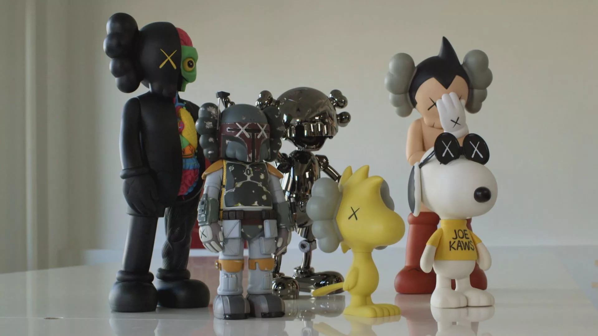 A collection of KAWS figurines, including a dissected Companion, Boba Fett, Astro Boy on Snoopy, and a chrome Companion, displayed on a white surface