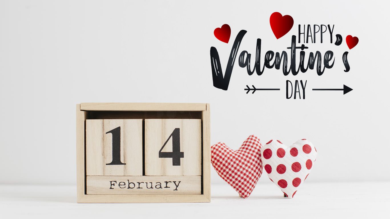 Valentine's Day decorations with a wooden calendar and two fabric hearts on a white table. Text reads 'Happy Valentine's Day'