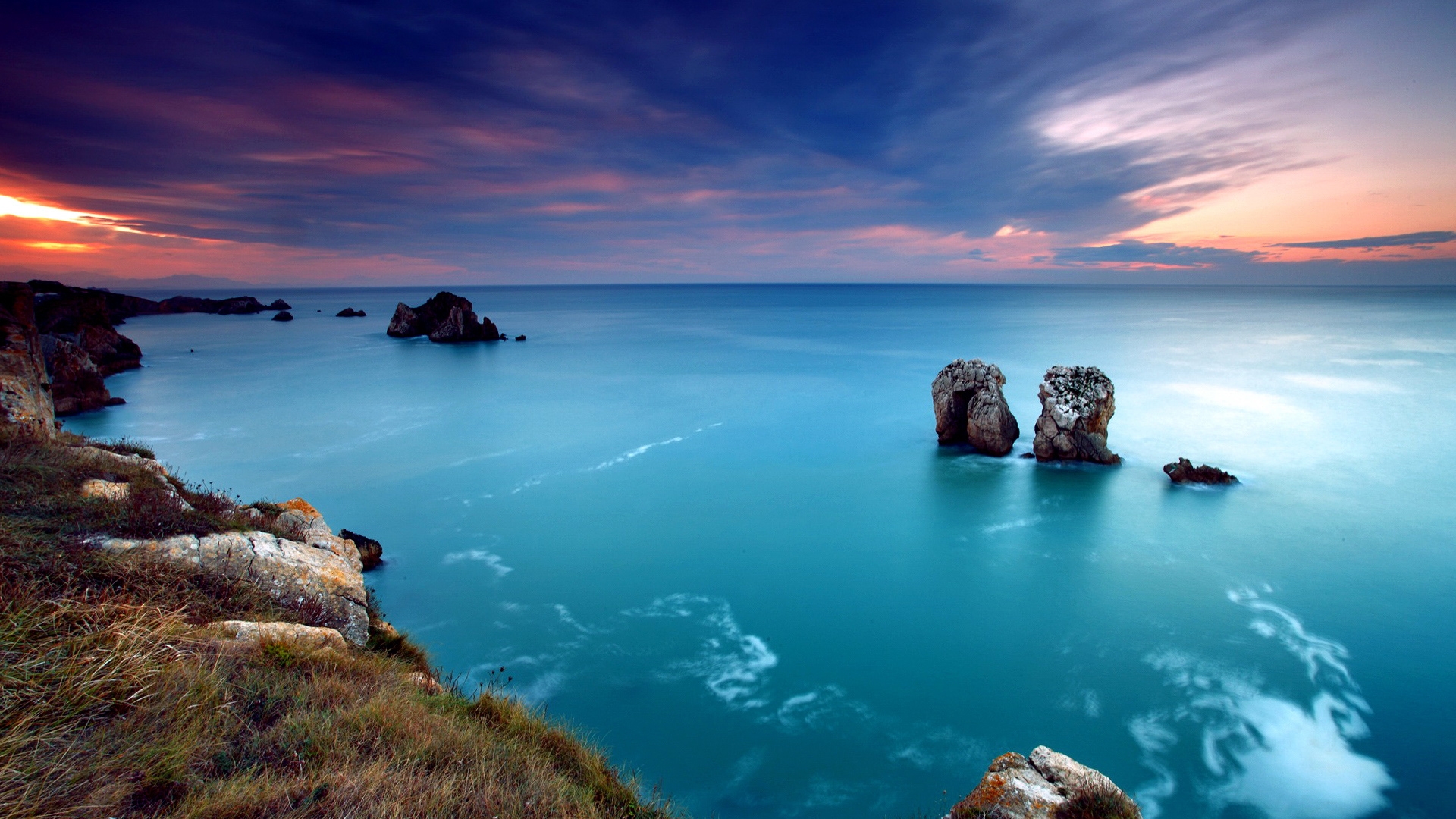 Stunning sunset over a tranquil ocean with rocky outcrops emerging from the water, evoking peace and serenity