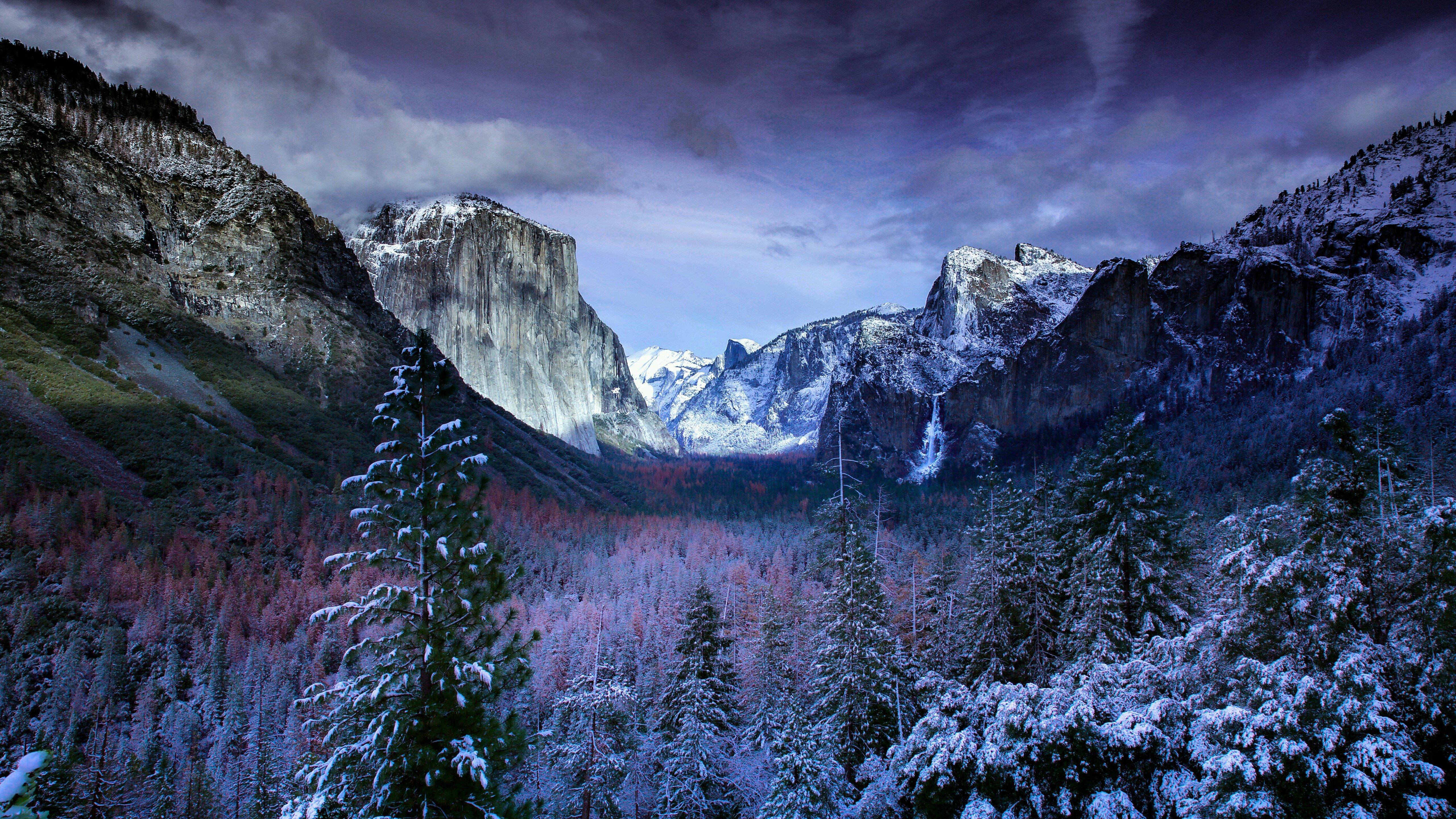A breathtaking 5K wallpaper showcasing a snow-covered Yosemite Valley, featuring El Capitan and Half Dome, under a dramatic purple sky