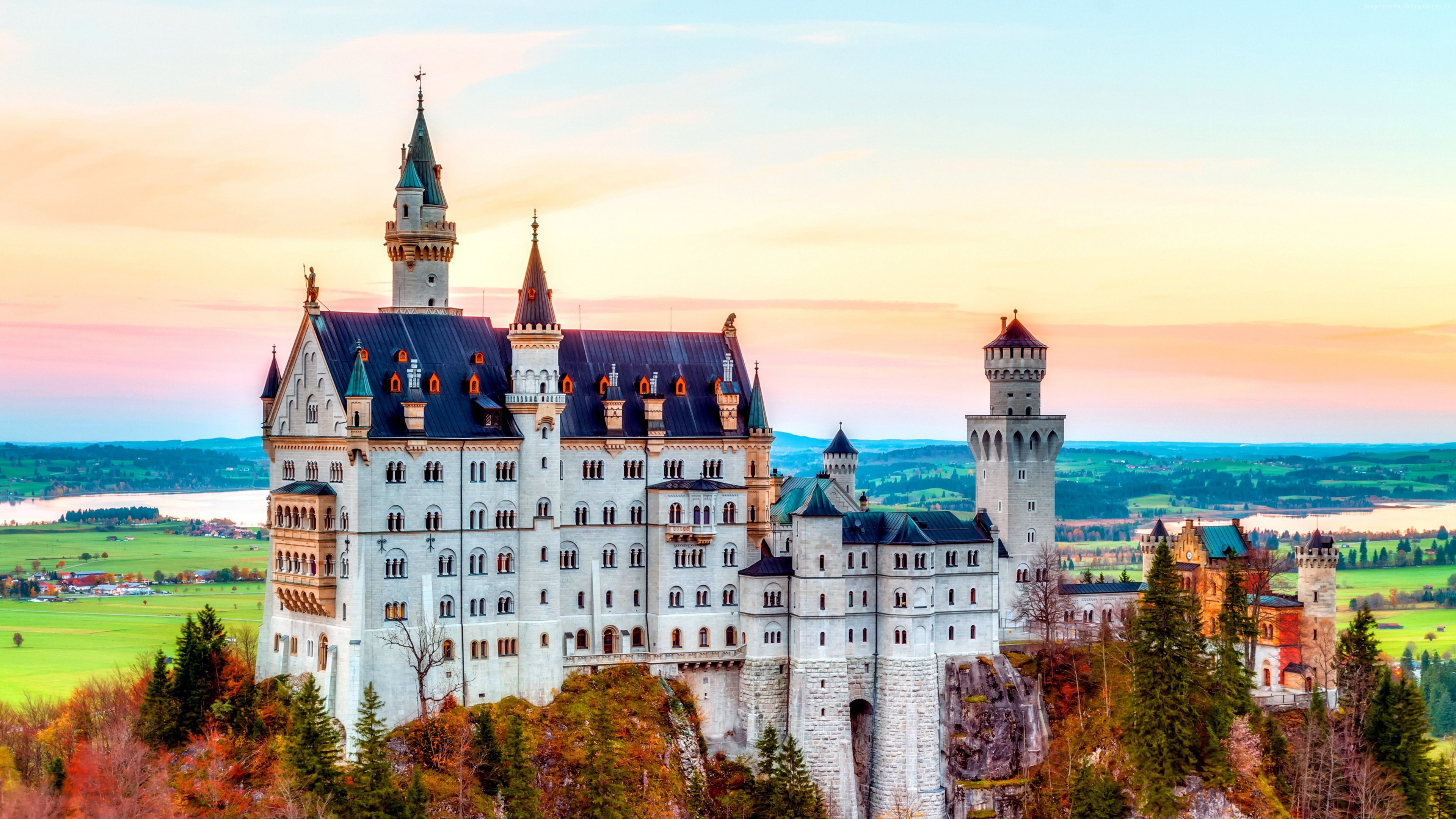 Neuschwanstein Castle in Germany at sunset, a fairytale castle perched on a rugged cliff overlooking a picturesque valley