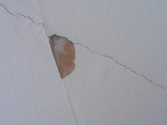 Wall crack not through gray surface but showing seam brown paper
