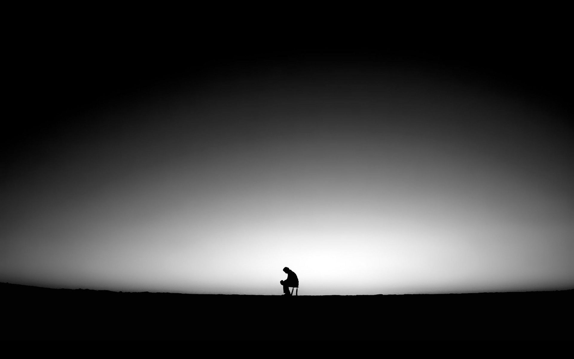 A lone silhouette sits hunched over on a chair against a stark, gradient backdrop of light and shadow, evoking feelings of solitude and contemplation