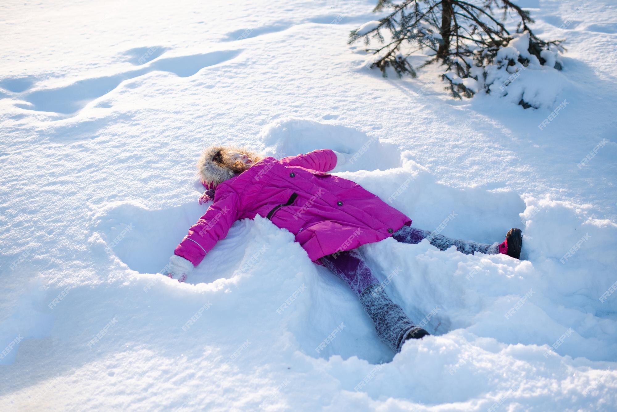 A child dressed in a pink winter coat makes a snow angel in fresh snow
