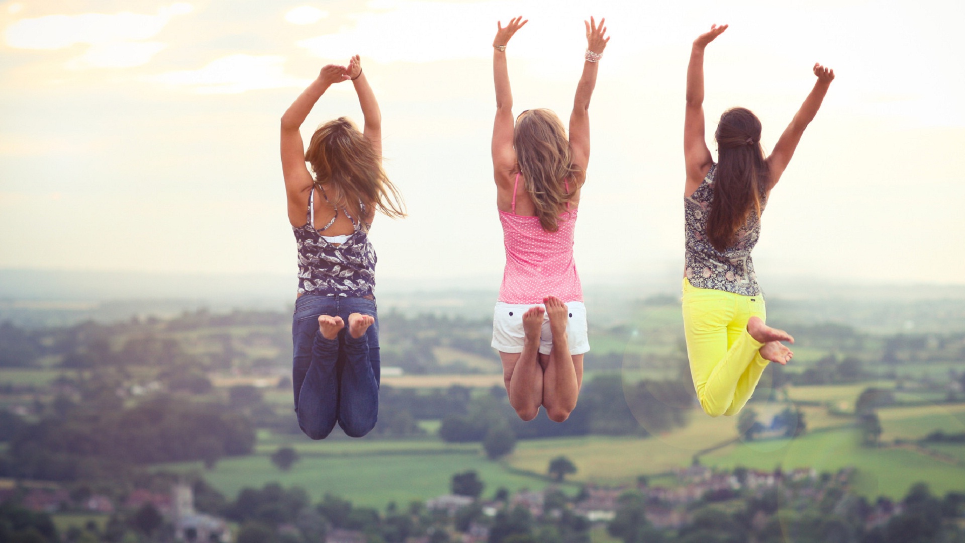 Three friends jumping for joy with a picturesque countryside backdrop, celebrating their friendship