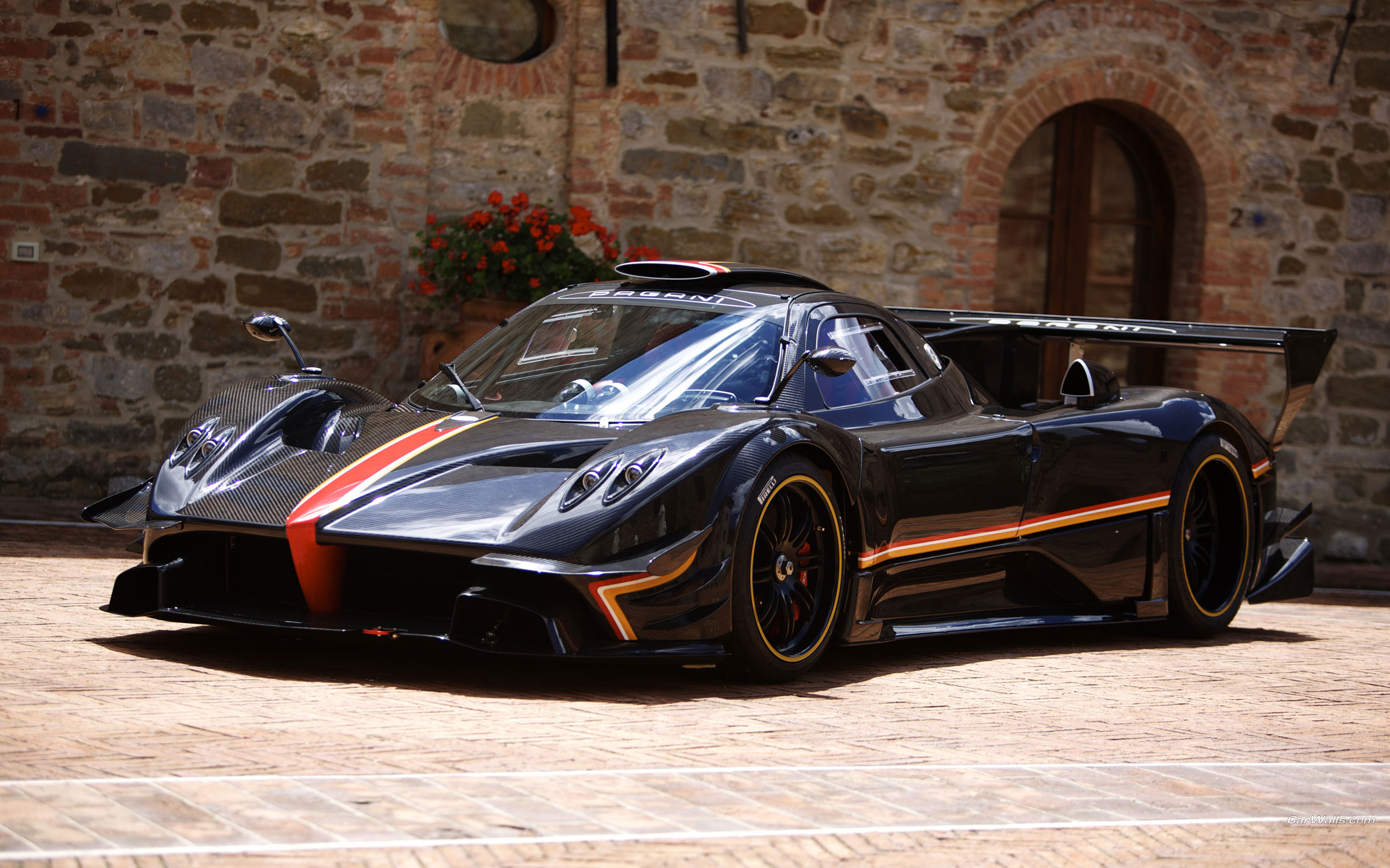 A sleek black Pagani Zonda supercar parked in front of a stone building