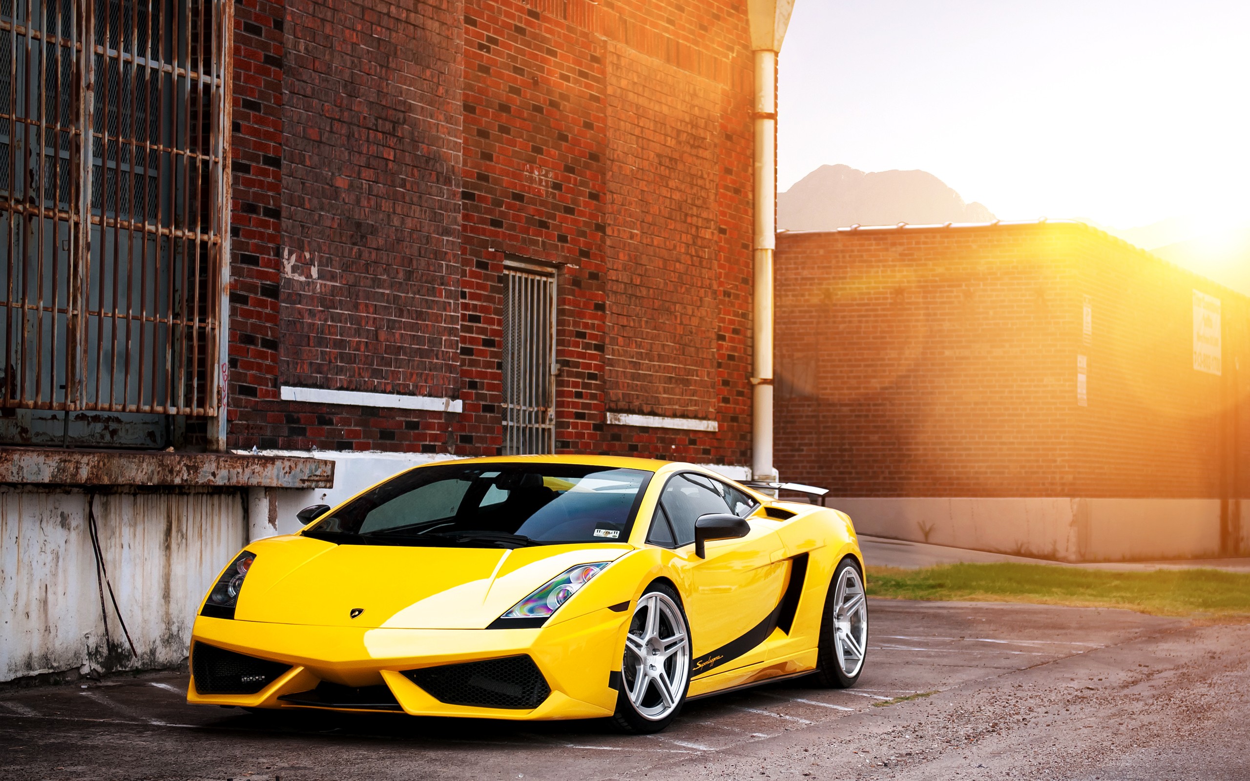 A vibrant yellow Lamborghini Gallardo parked against a brick wall, bathed in the warm glow of the setting sun