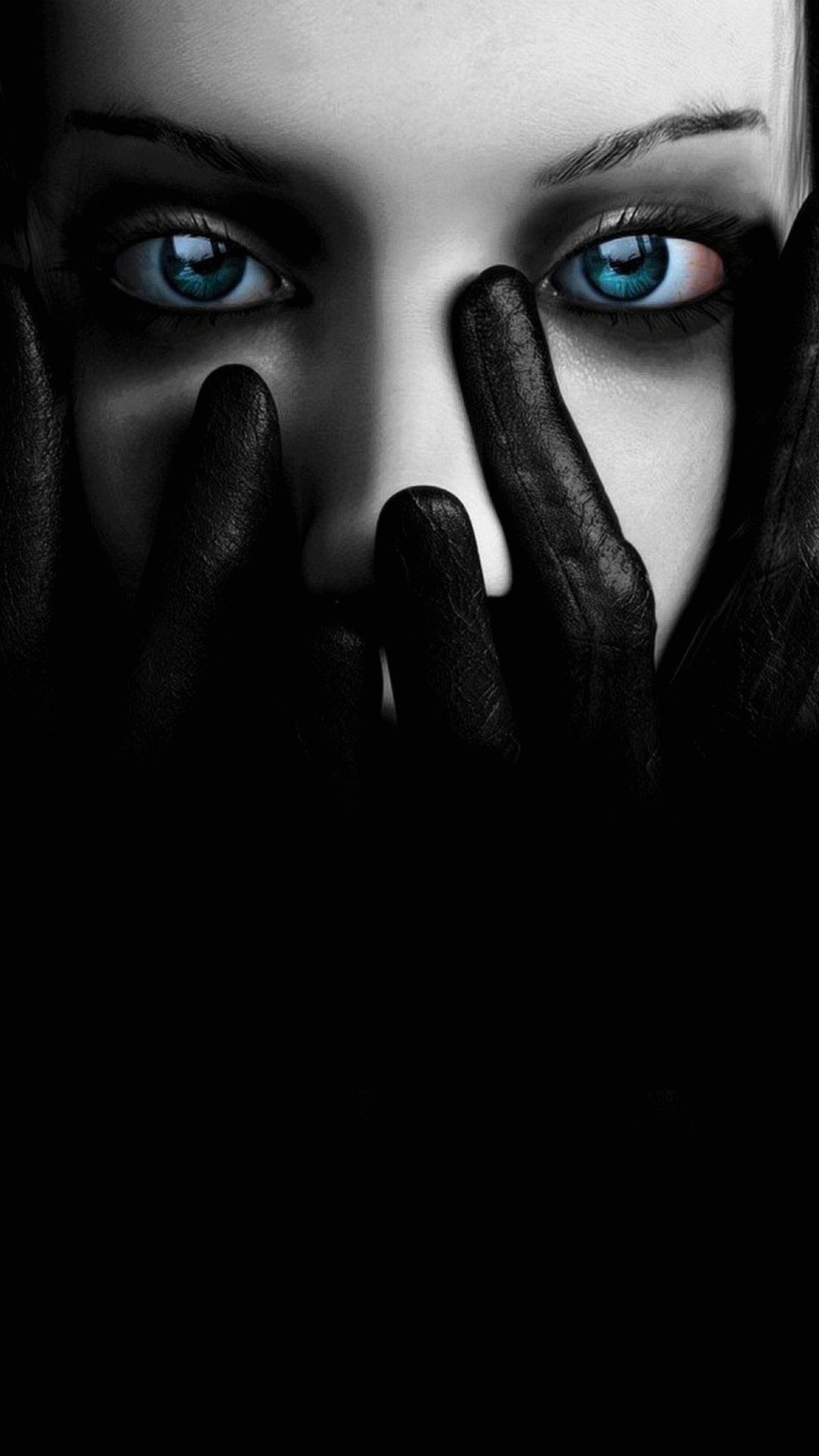 Close-up of a person's face with striking blue eyes, partially obscured by black gloves, creating a dramatic and mysterious effect. Suitable for a phone wallpaper