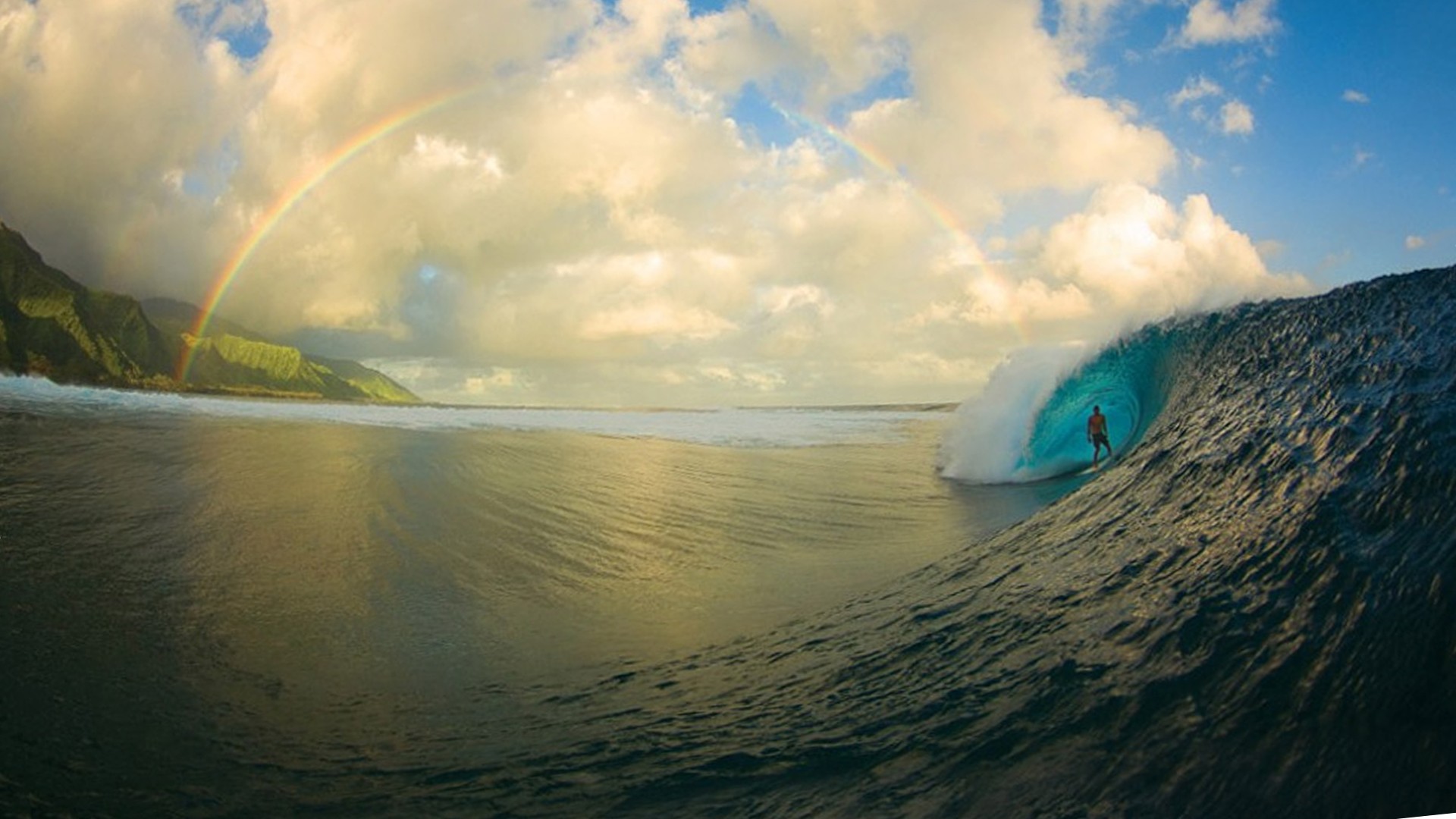 A surfer rides a perfect wave under a rainbow in a stunning surfing wallpaper scene