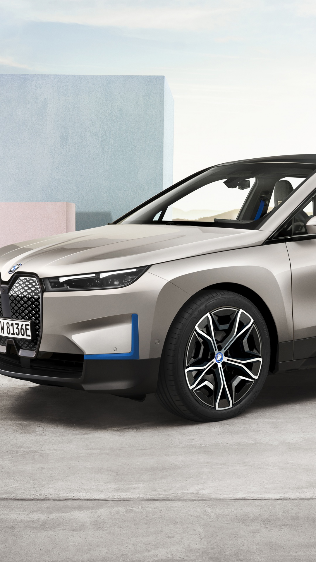 Close-up front view of a silver BMW iX electric SUV, highlighting its modern design, illuminated headlights, and unique wheel rims