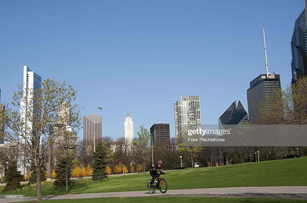 Cyclists In Millenium Park With Chicago Skyline Background High