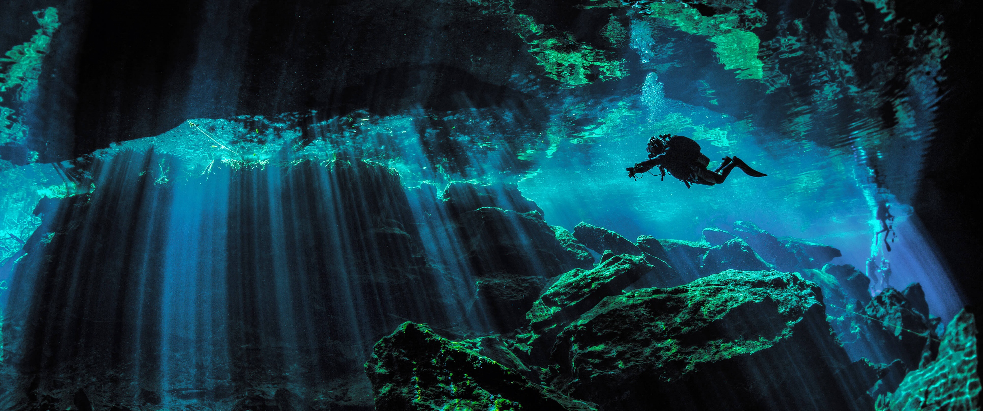 Scuba diver explores a mesmerizing underwater cave illuminated by beams of sunlight