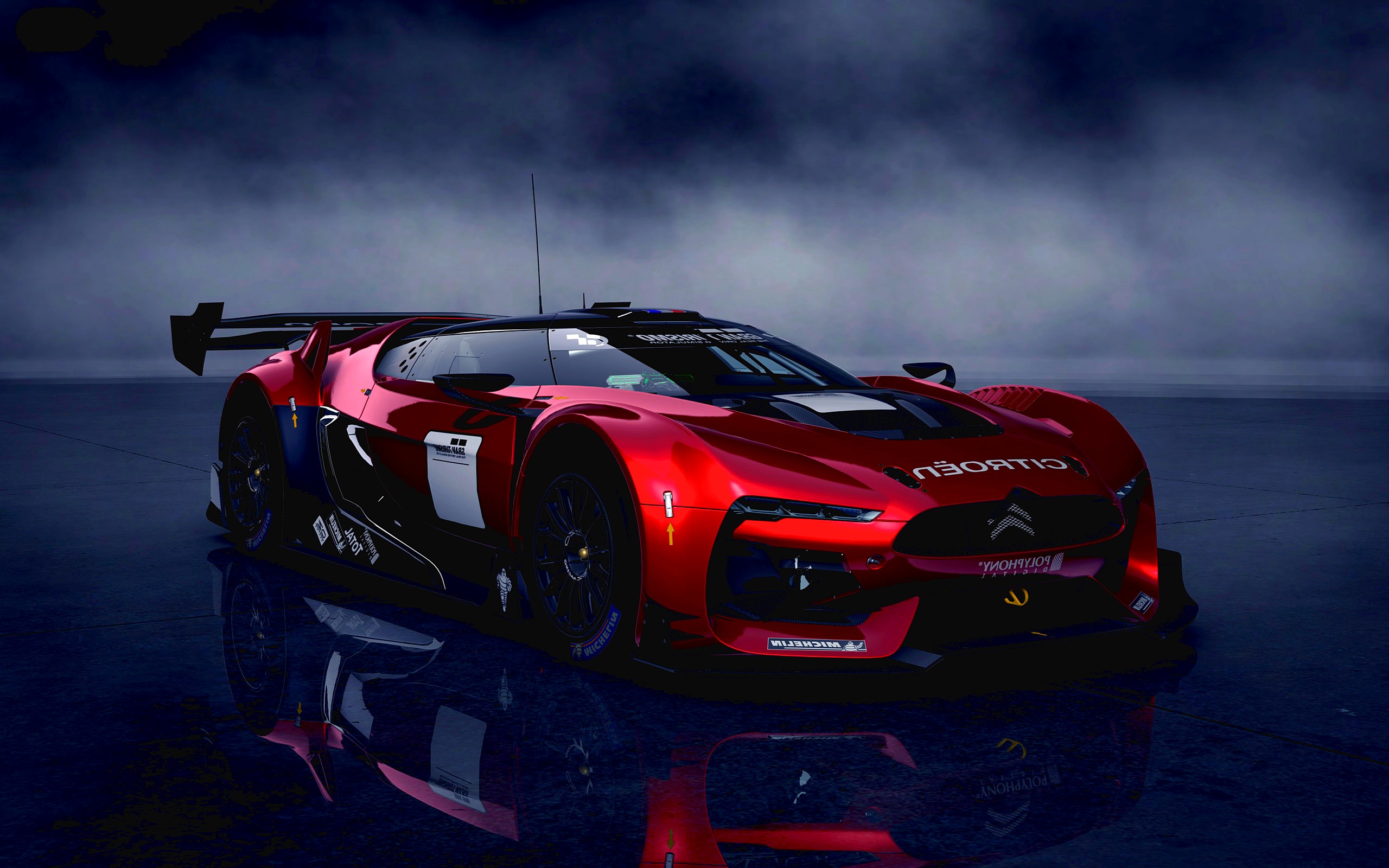 A sleek, red Citroen GT concept car parked on a dark, reflective surface, possibly a wet track. The car features racing details such as a large spoiler and sponsor decals. Its futuristic design and vibrant color stand out against the moody backdrop