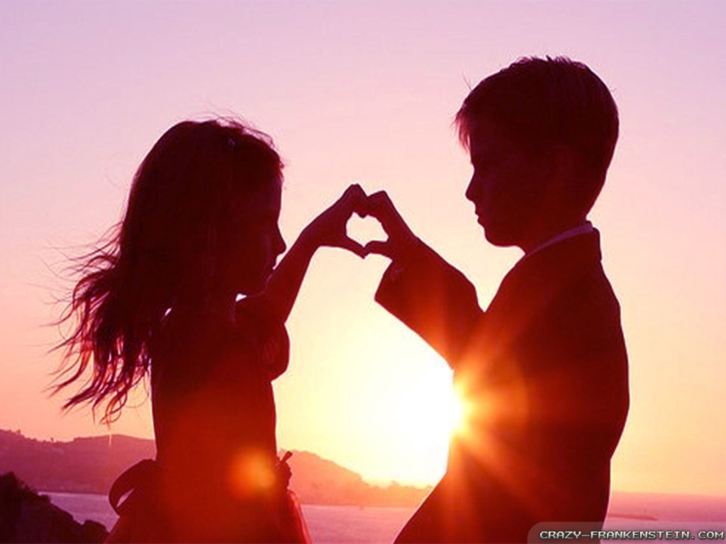 Silhouette of a young boy and girl making a heart shape with their hands against a sunset backdrop