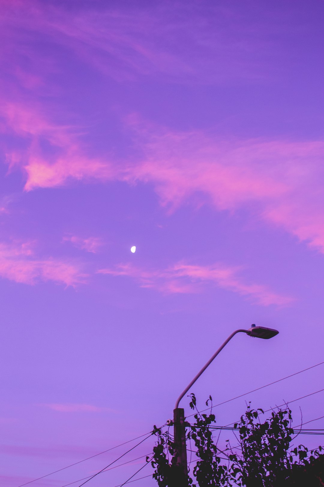 A captivating purple sunset sky with a crescent moon and a silhouetted streetlight in the foreground. Perfect for purple aesthetic wallpapers