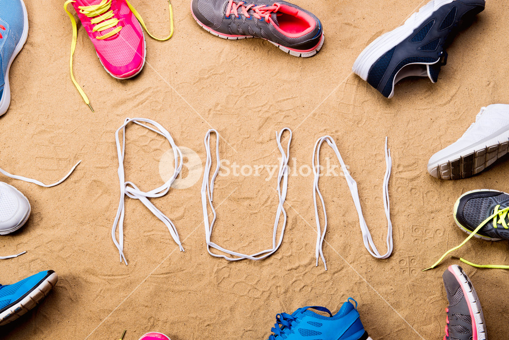 Various Running Shoes And Run Sign Made Of Shoelaces Against Sand
