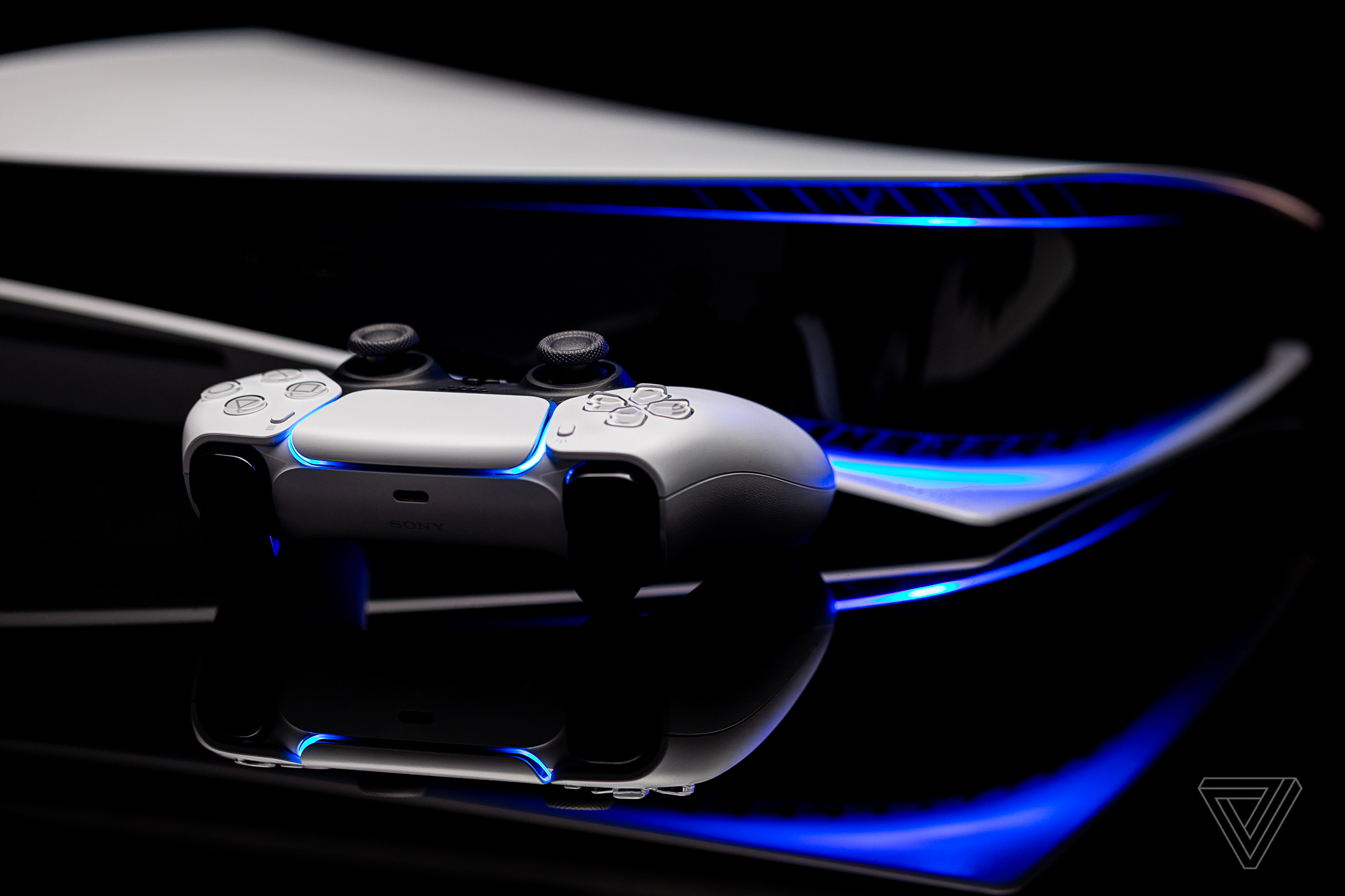 A PlayStation 5 console with its DualSense controller, illuminated by blue light, against a dark background