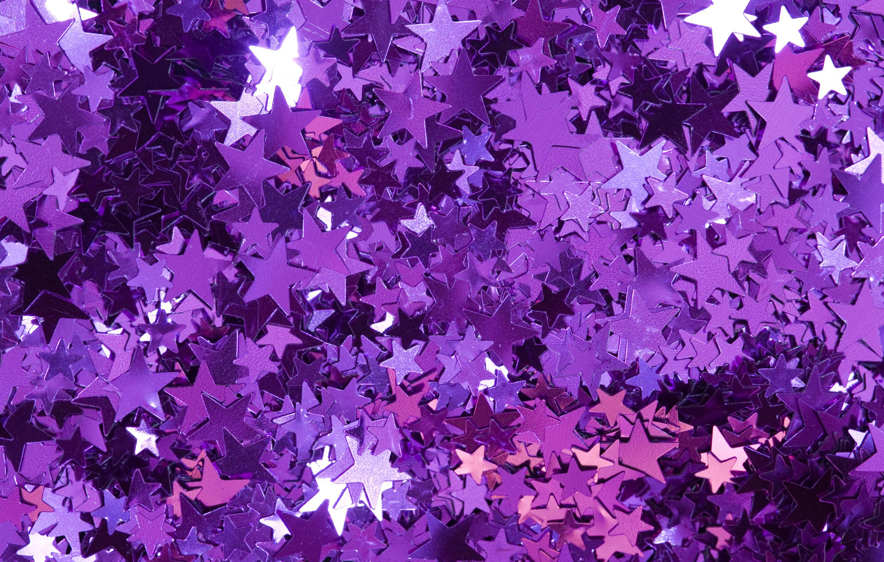 A close-up view of a pile of small, shiny, metallic purple star confetti, creating a sparkly and festive background