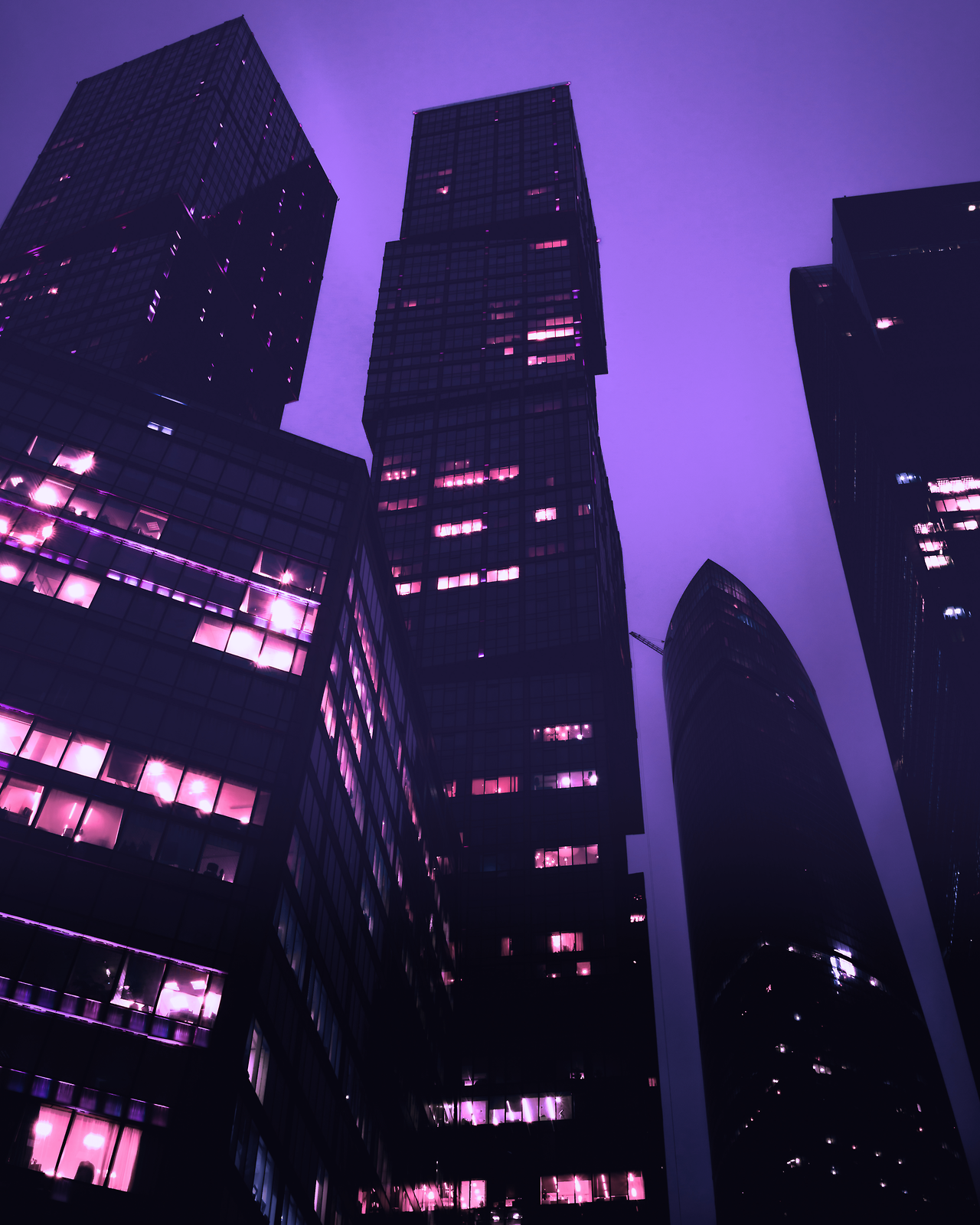 Low-angle view of modern skyscrapers at dusk, illuminated in vibrant purple hues, creating a futuristic cityscape aesthetic