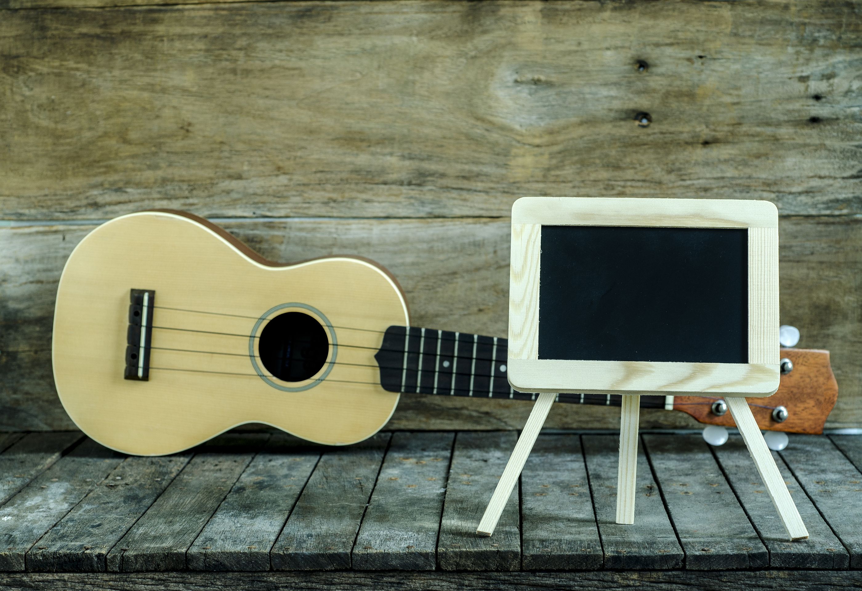 Ukulele Guitar And Blank Blackboard On Wooden Background
