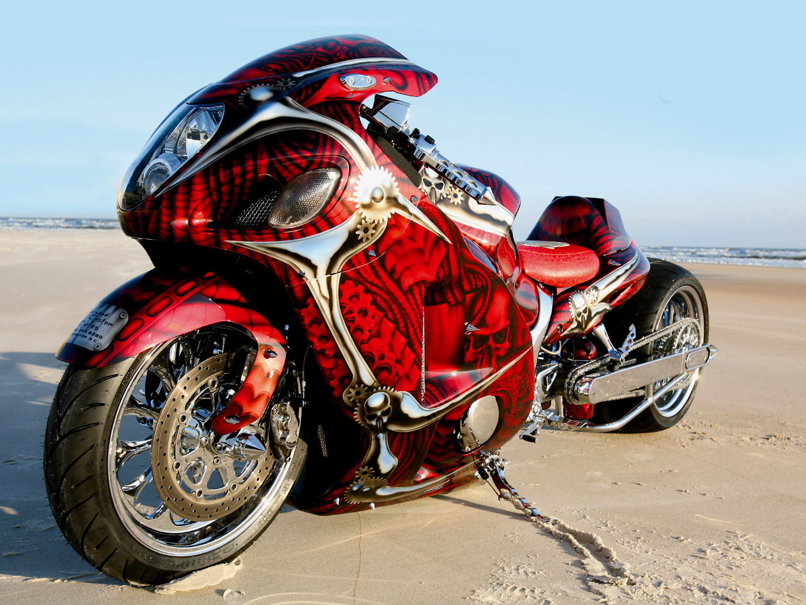Custom-painted red and silver motorcycle on a sandy beach, showcasing intricate details and modifications