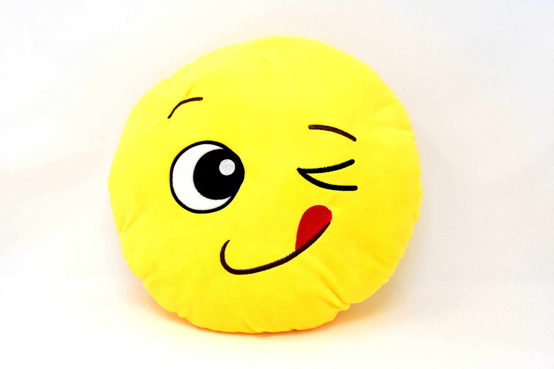 A plush yellow emoji pillow winks and sticks its tongue out, perfect for adding a playful touch to any space