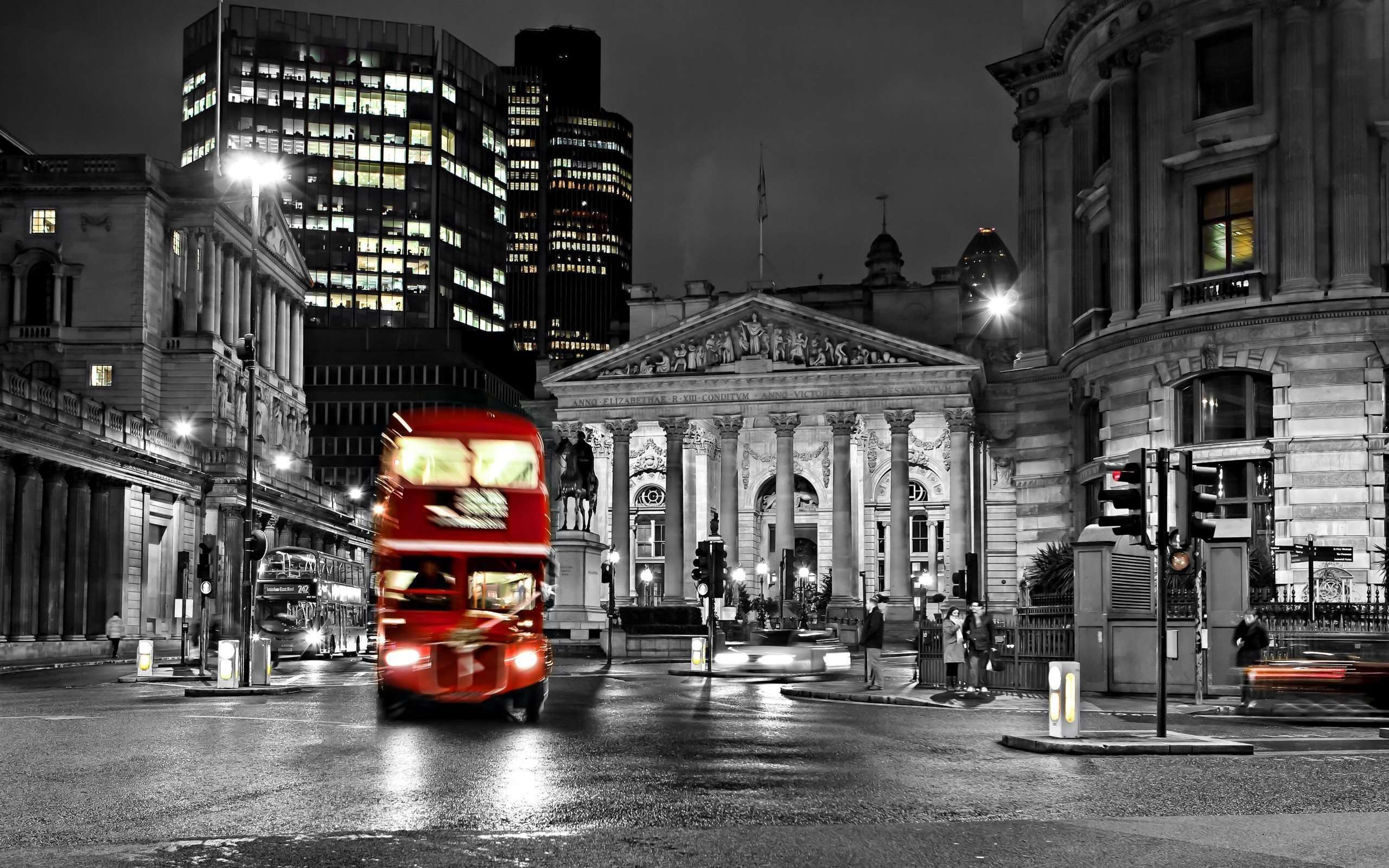 A vibrant red double-decker bus in motion against a monochrome backdrop of London's iconic architecture at night
