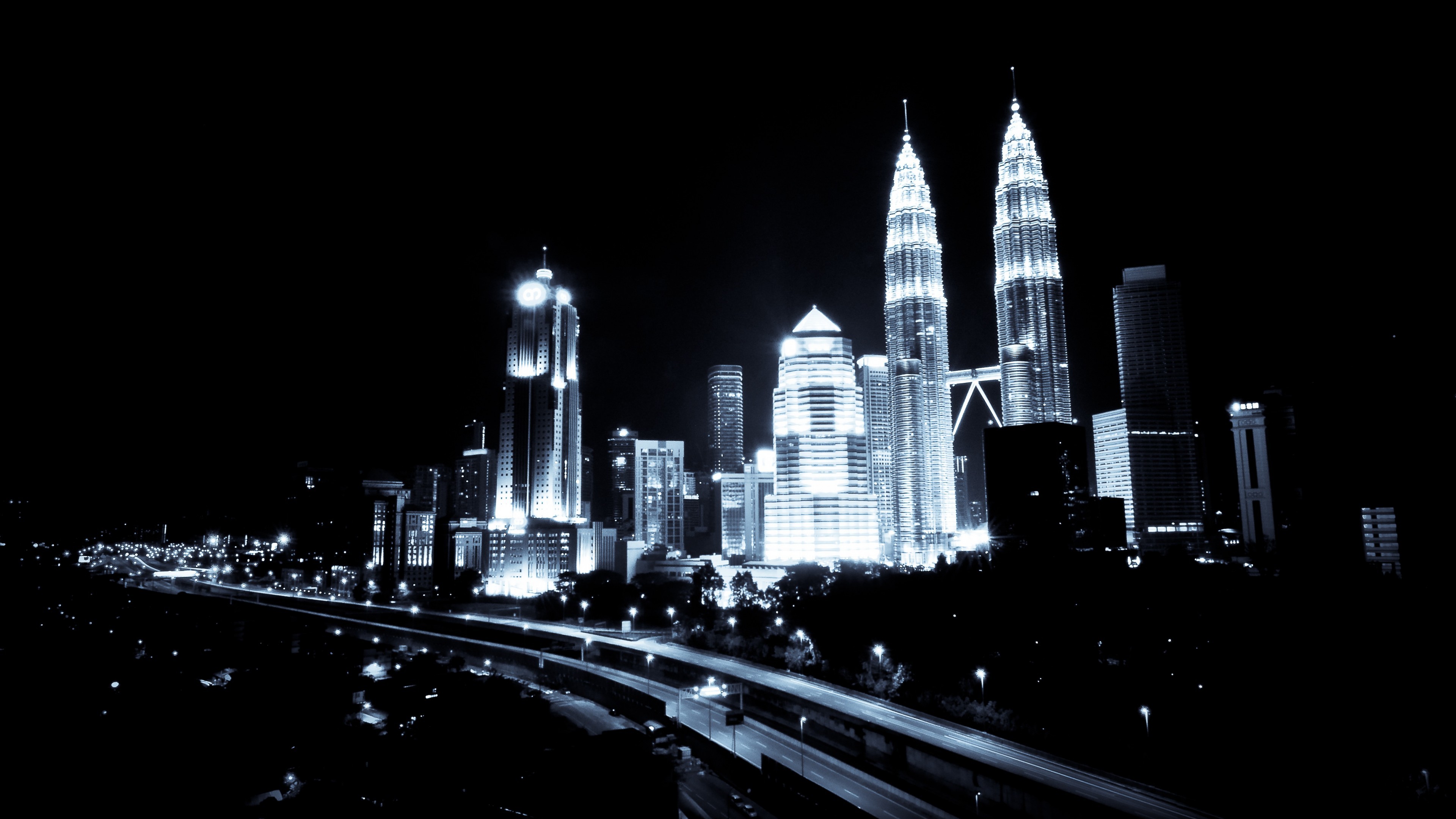 Black and white night view of Kuala Lumpur city skyline with illuminated skyscrapers and light trails on the highway, perfect for a 4k wallpaper