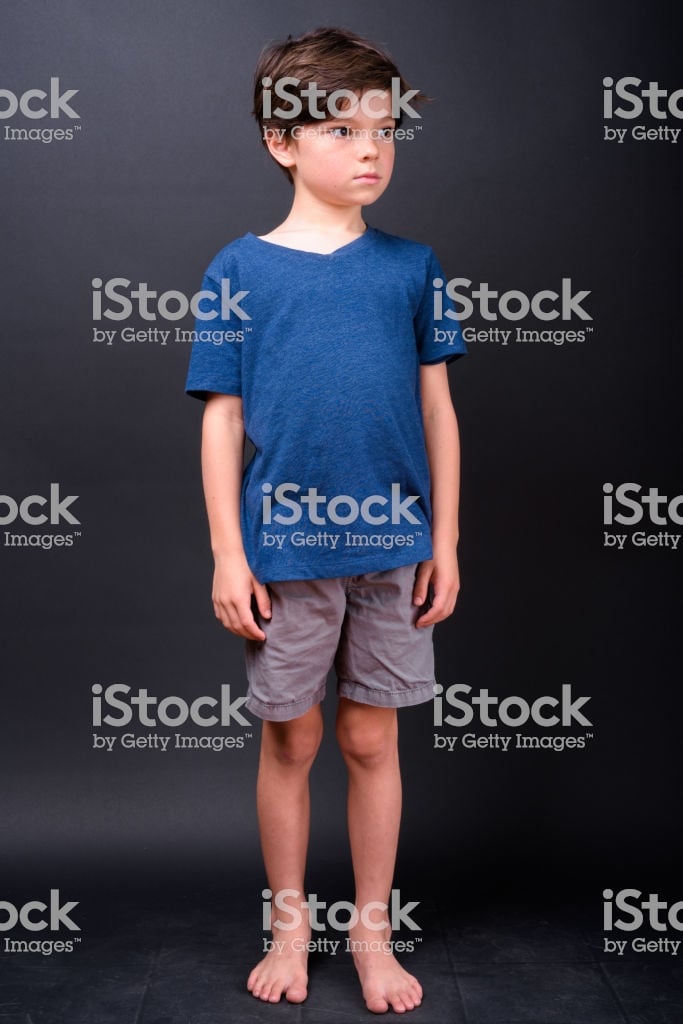 Portrait Of Cute Boy Standing Barefoot Against Black Background
