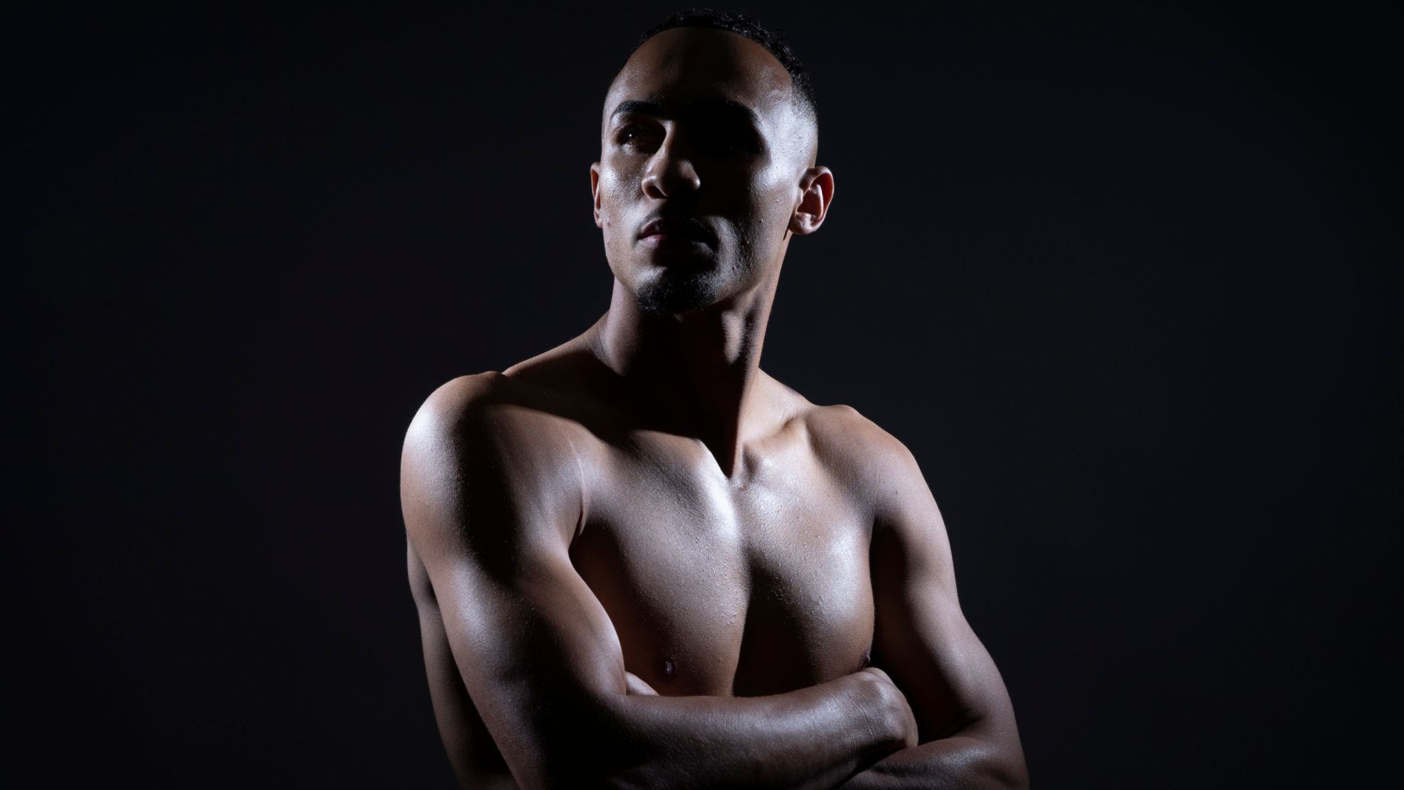 Benjamin Whittaker posing shirtless with arms crossed against a dark background