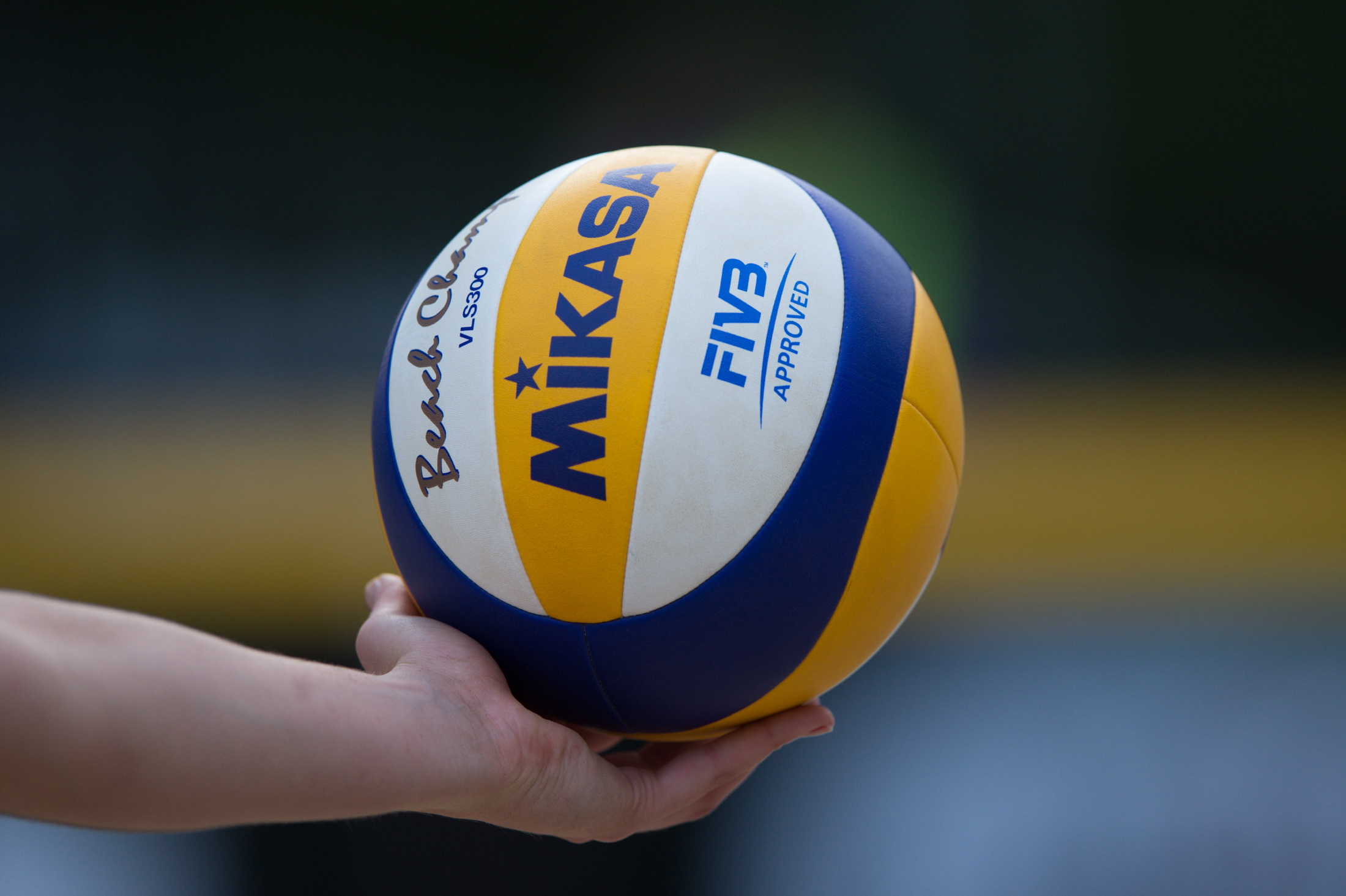 A close-up of a hand holding a Mikasa beach volleyball against a blurred background