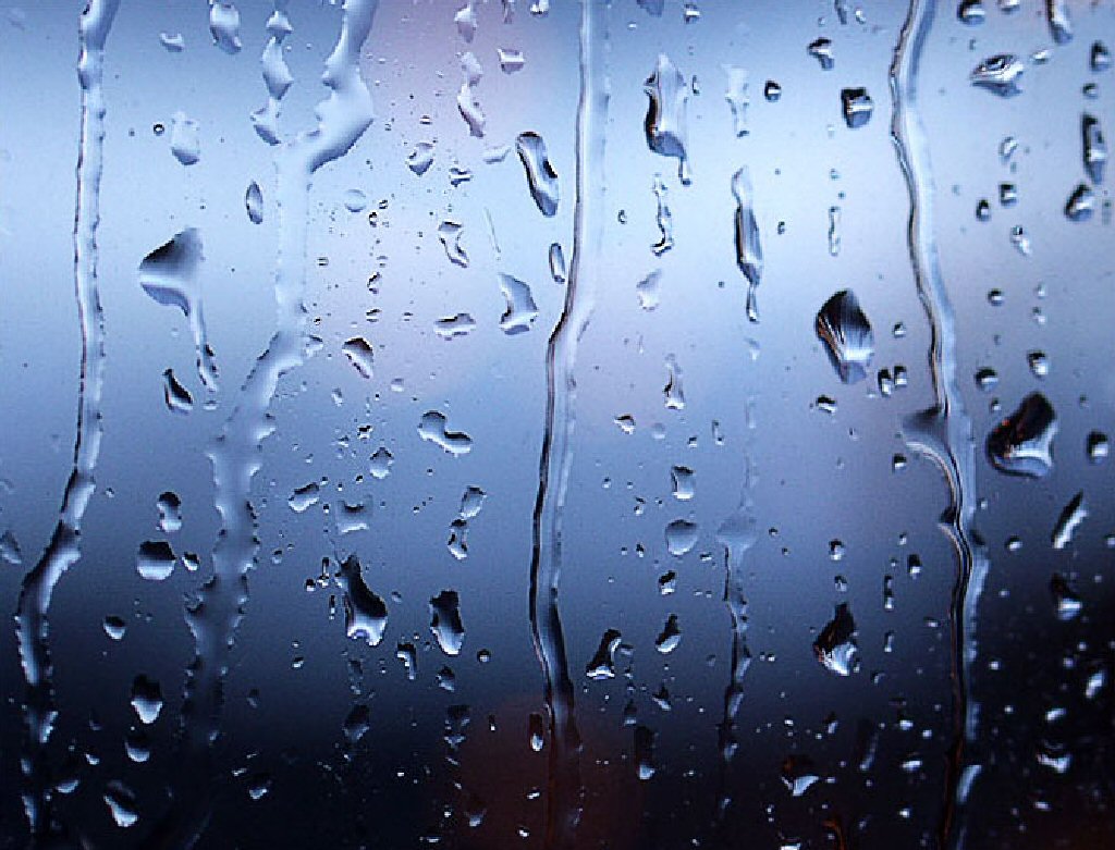 Close-up of raindrops on a window pane, creating a textured, abstract pattern against a blurred background