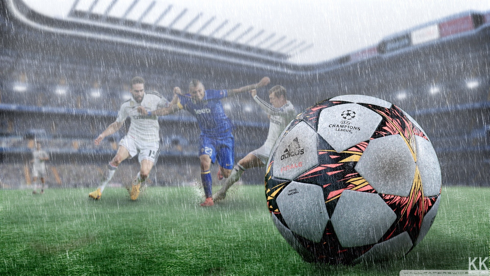 A Champions League soccer ball in the foreground with a blurred image of a soccer game being played in the rain in the background