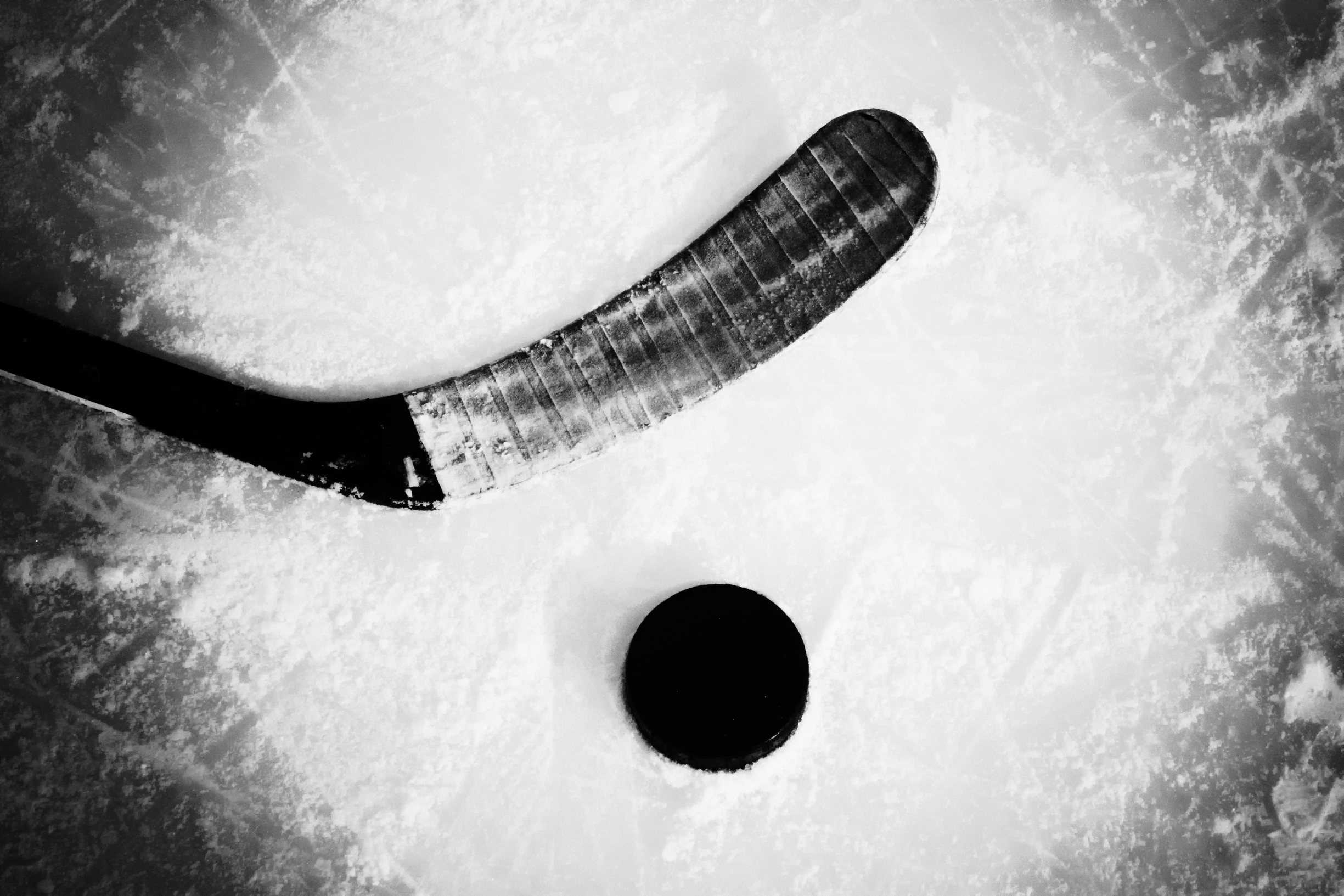 Black and white close-up of a hockey stick and puck on ice