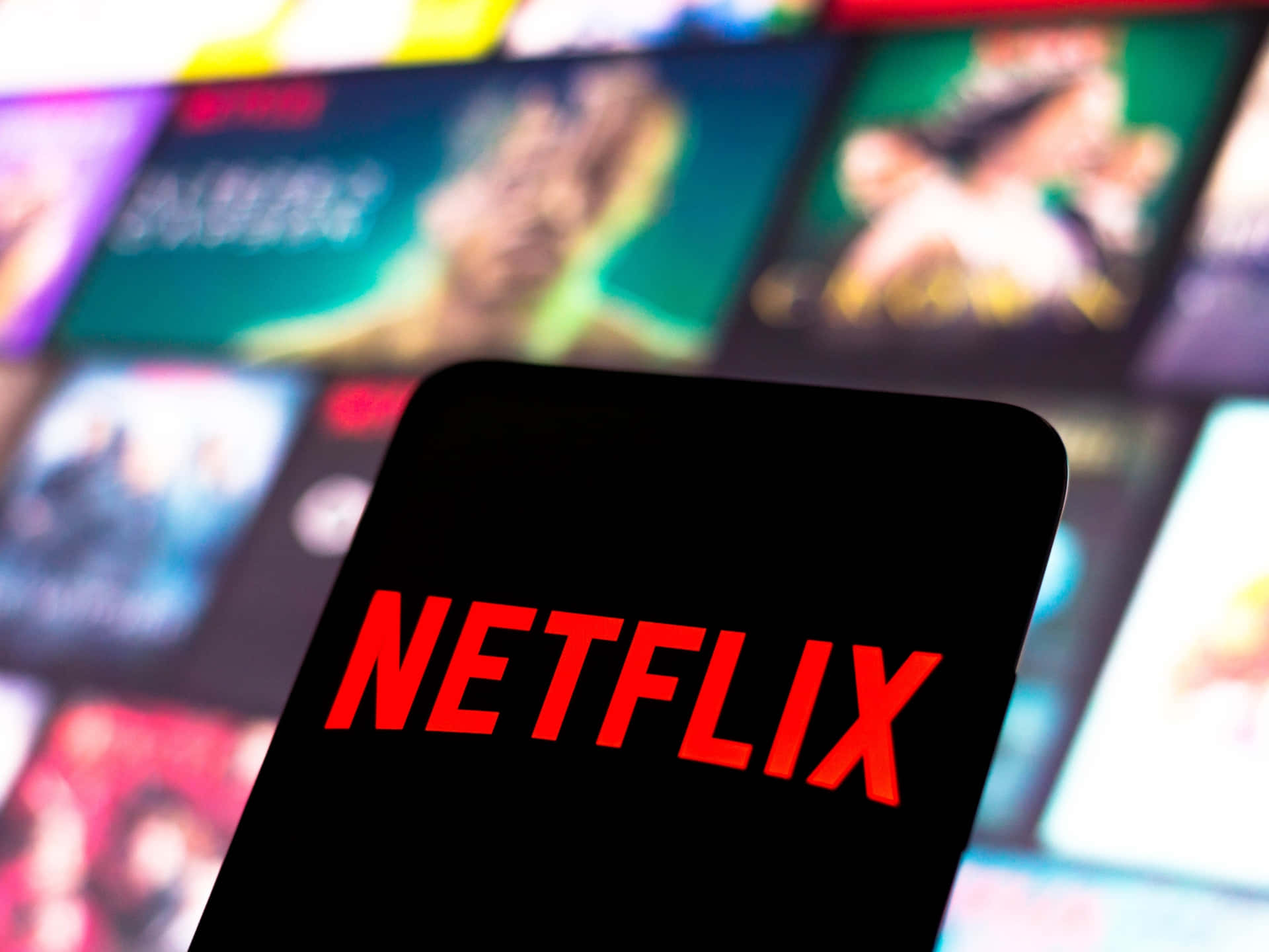 Netflix logo displayed on a phone screen, with a blurred background of Netflix show thumbnails
