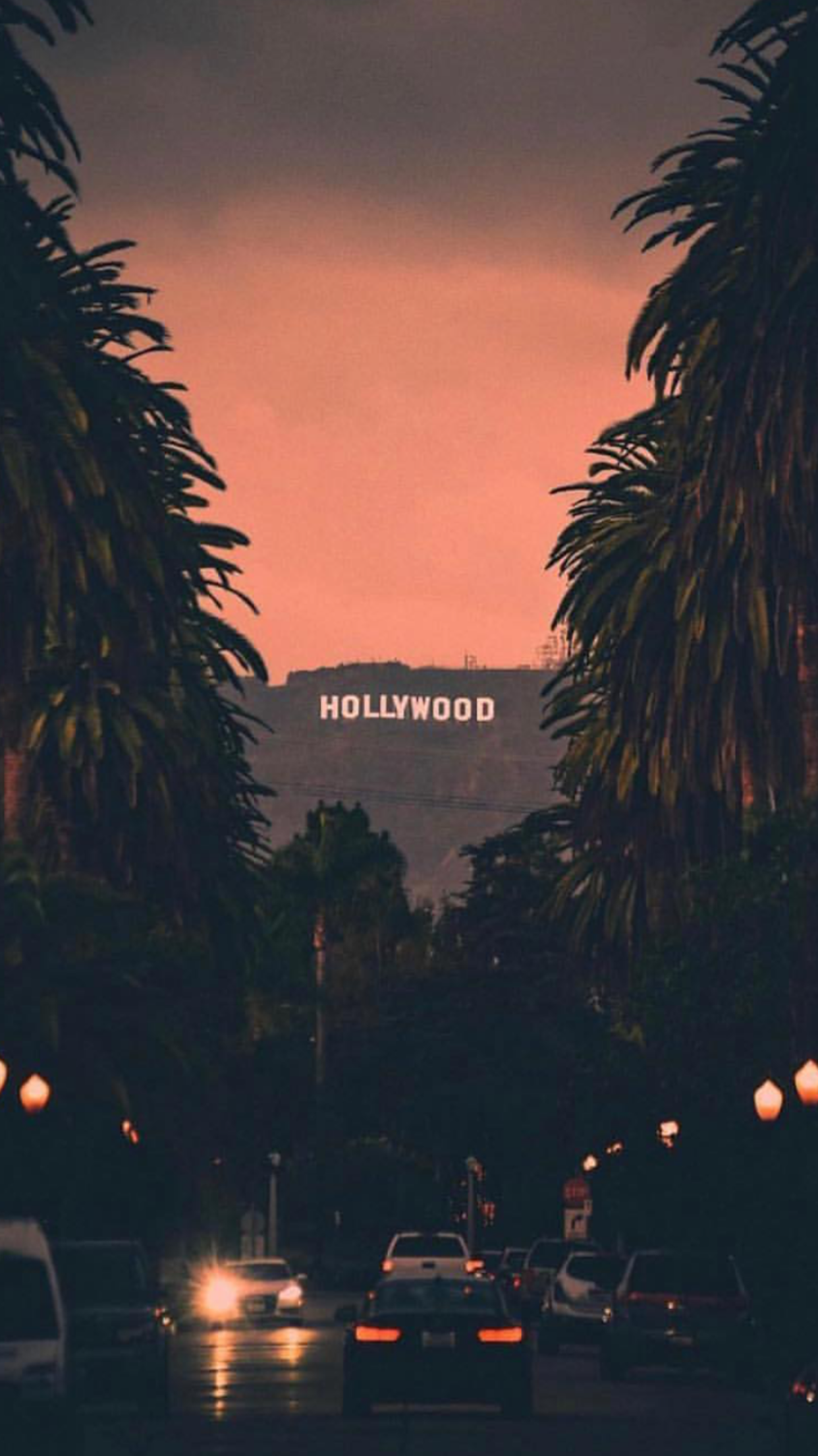 A captivating view of the iconic Hollywood sign at sunset, seen from a bustling street lined with palm trees