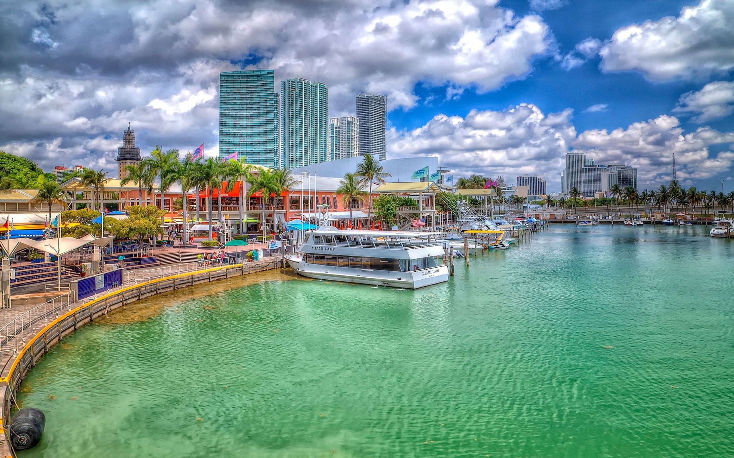 Scenic view of Miami's waterfront with colorful buildings, palm trees, boats, and the city skyline under a vibrant sky