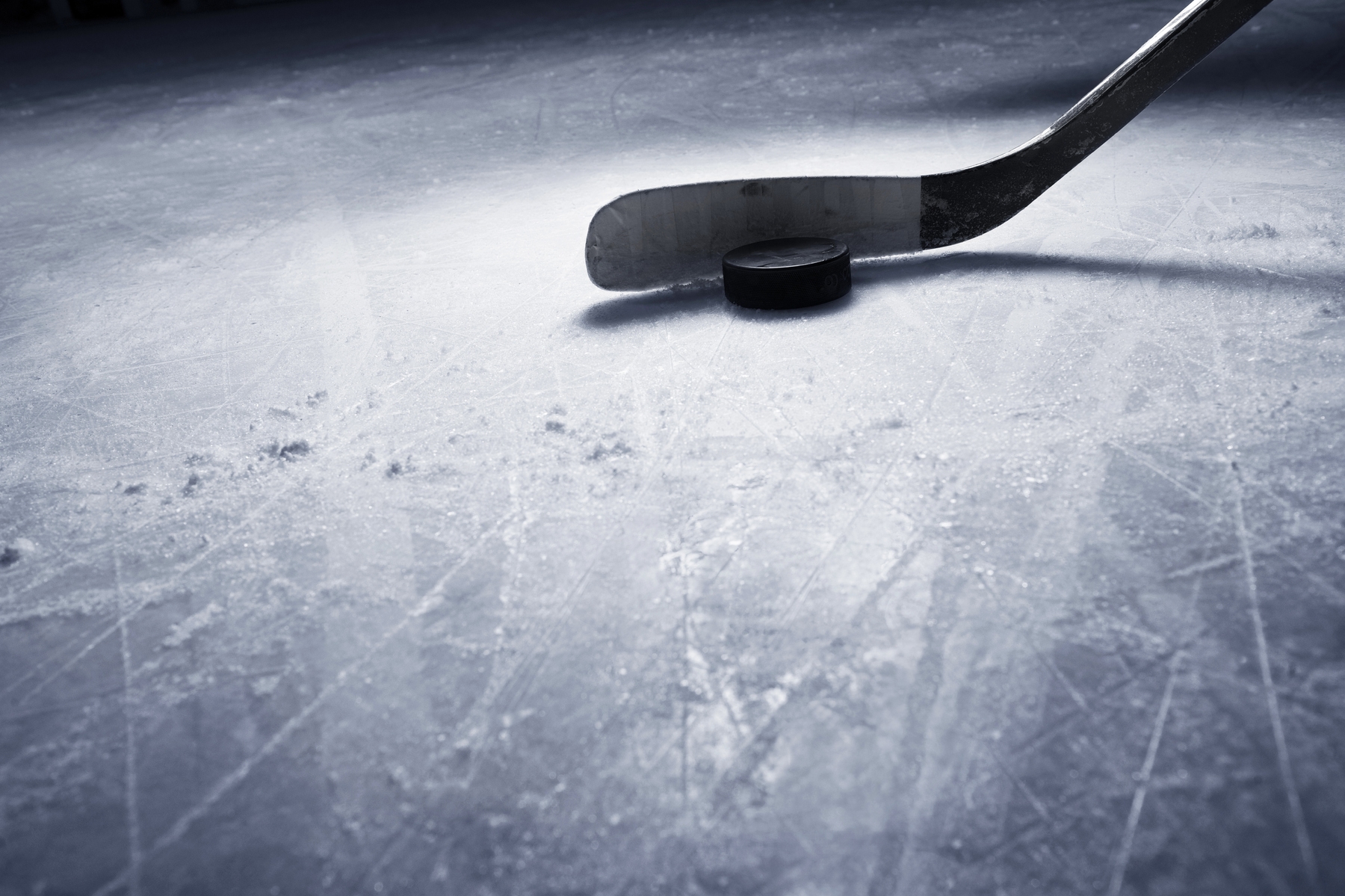 A hockey puck and stick on a scratched ice rink surface, ready for action