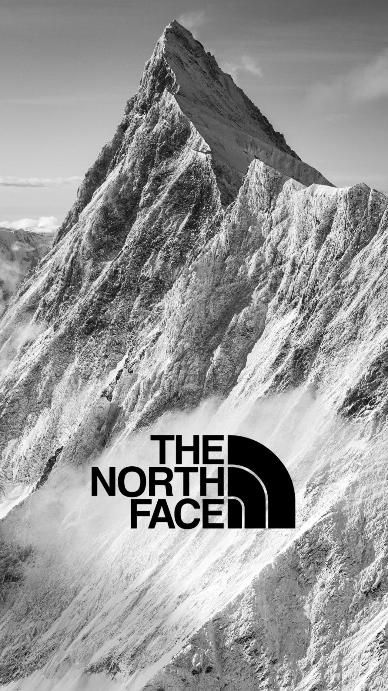 A stunning black and white photograph of a snow-capped mountain peak, showcasing the rugged beauty of nature. The iconic The North Face logo is subtly placed, hinting at the brand's connection to exploration and outdoor adventure