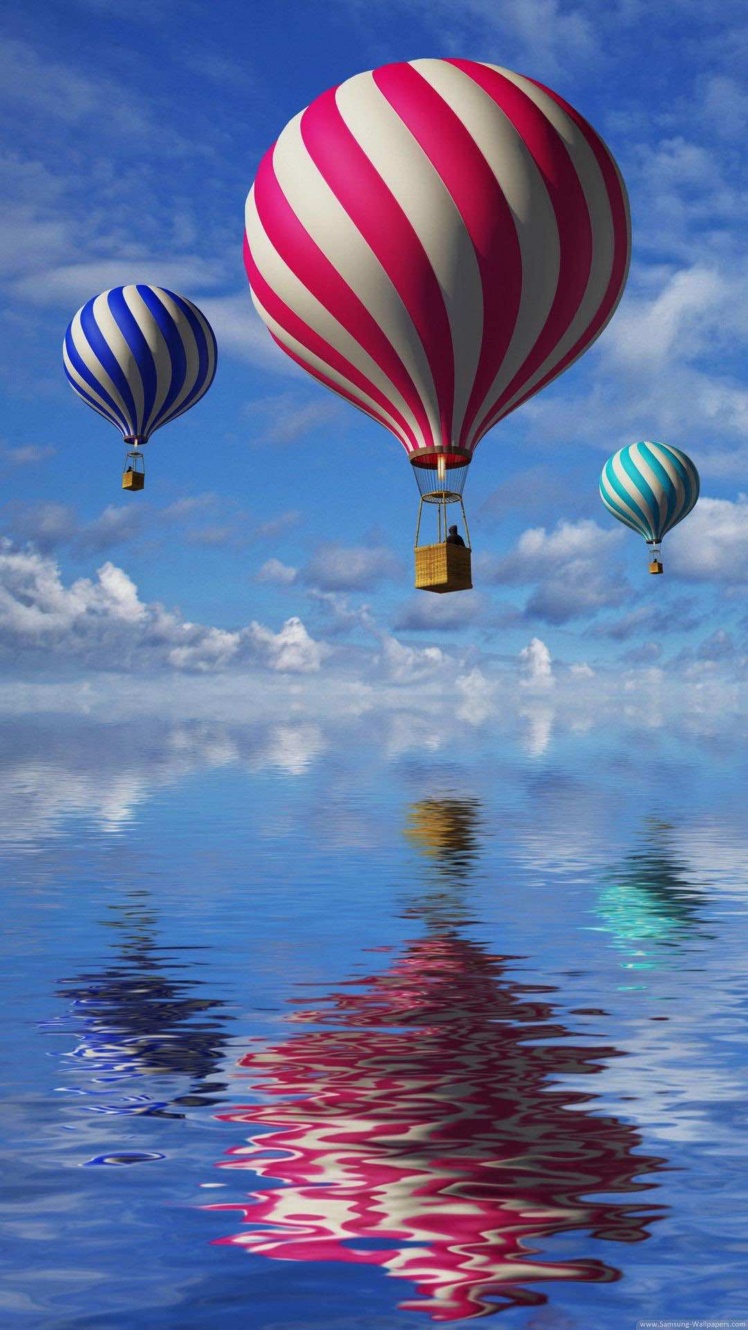 Three hot air balloons soaring over a tranquil body of water, reflecting in the surface below. The sky is a vibrant blue with scattered clouds