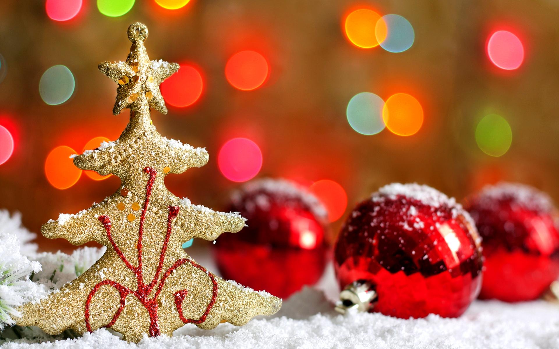Glittering gold Christmas tree ornament and red baubles dusted with snow against a backdrop of colorful bokeh lights