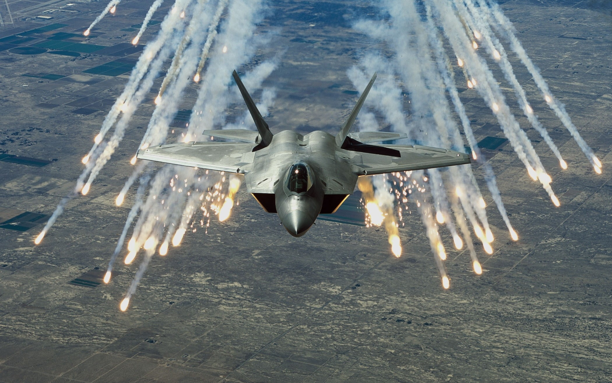 An F-22 Raptor deploying flares during a military exercise, creating a dramatic display against the desert landscape