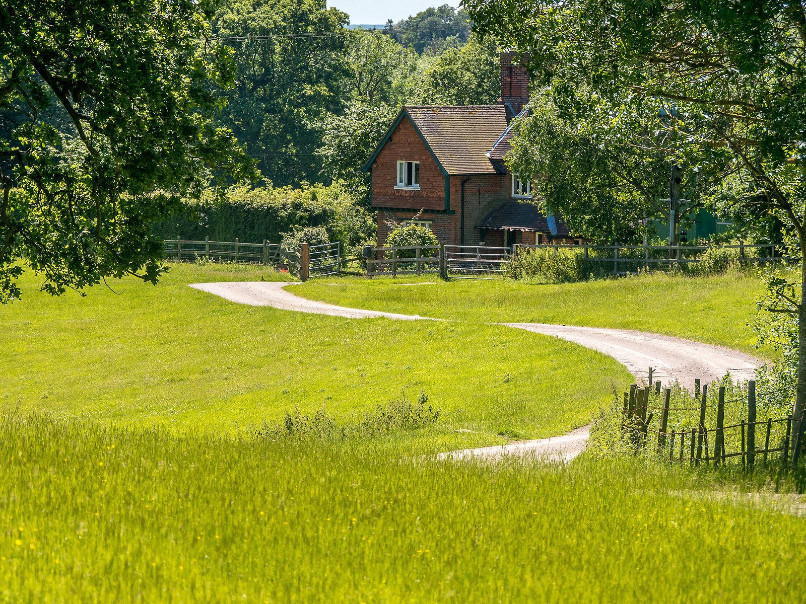 A House In The Middle Of Lush Green Field With Dirt Road Leading To It Wallpaper