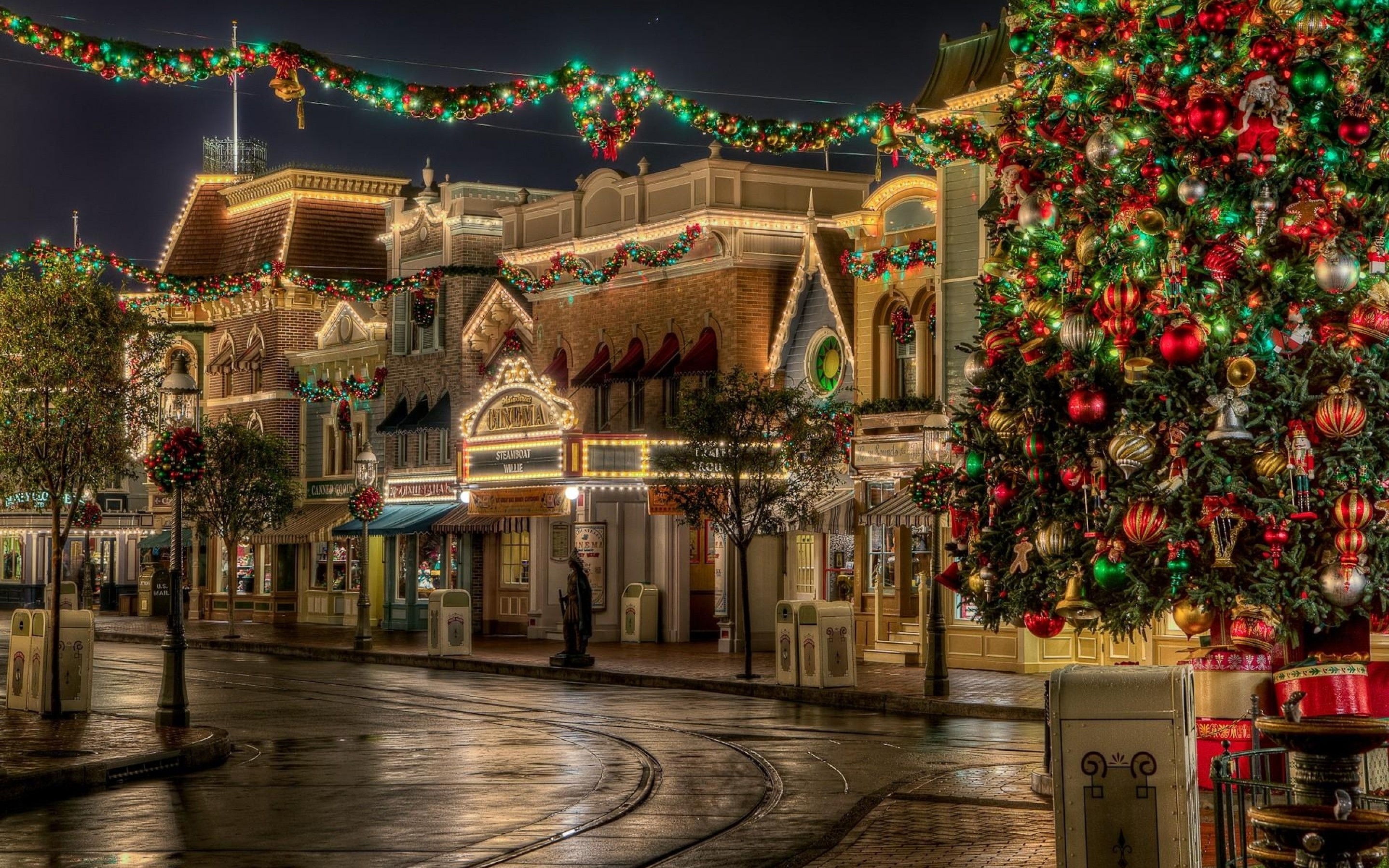 A Christmas tree decorated with lights and ornaments stands on a street lined with festive shops, evoking the warm, magical atmosphere of Christmas