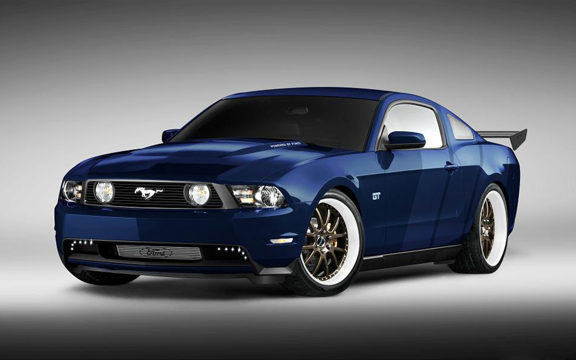 A customized, dark blue Ford Mustang GT with whitewall tires, a rear spoiler, and aftermarket body kit, parked against a gradient background
