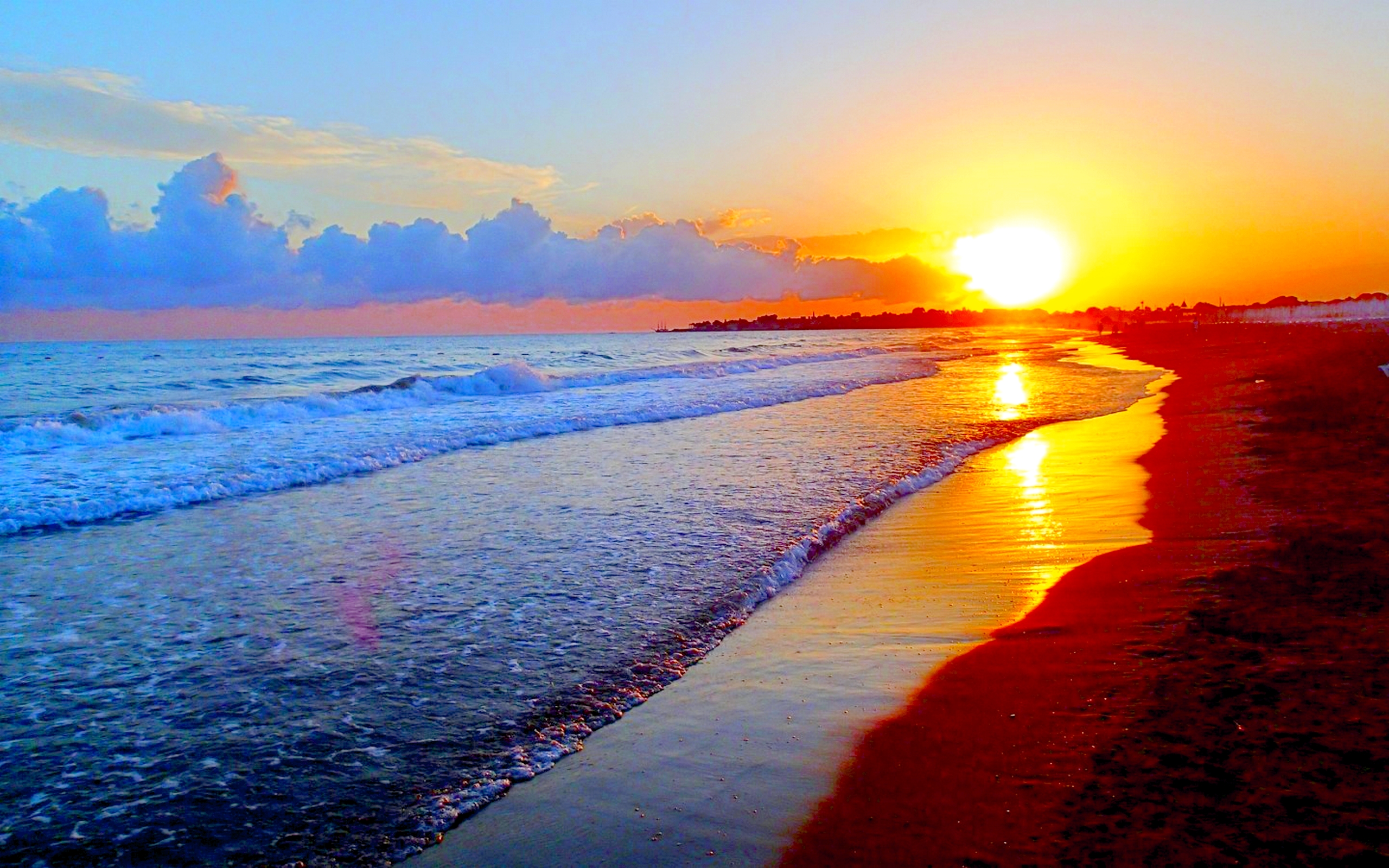 Vivid sunset over a tranquil beach, casting a warm golden glow on the sand and waves. Perfect for a desktop wallpaper