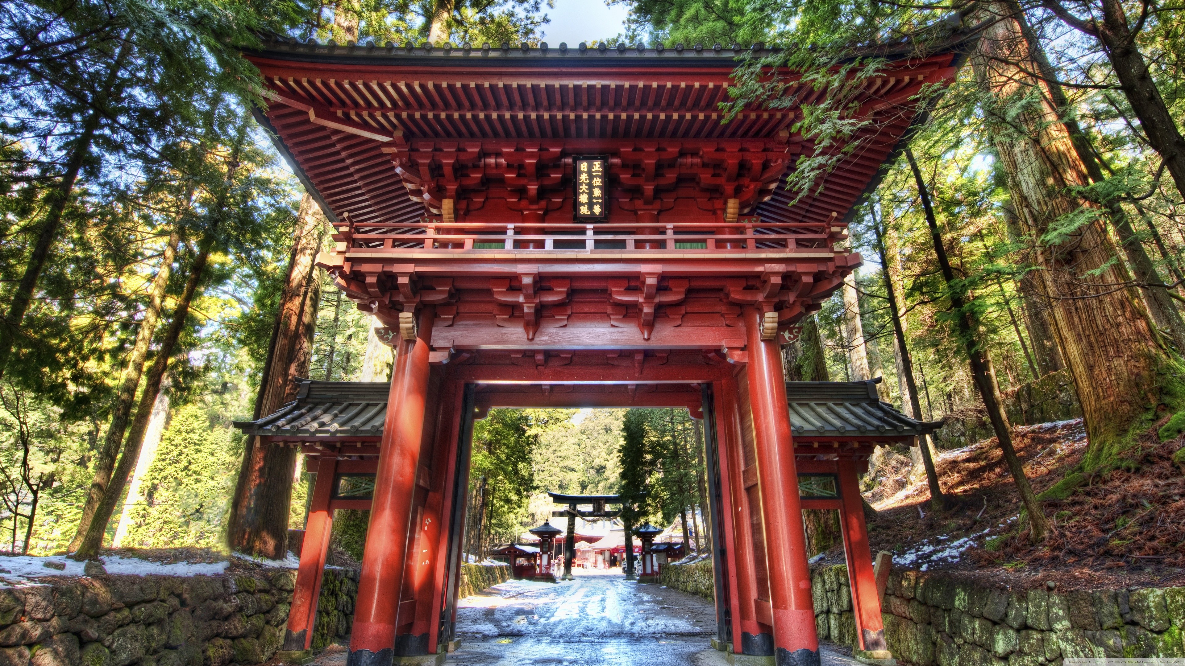 A vibrant red Japanese temple gate stands majestically amidst a serene forest, its traditional architecture contrasting beautifully with the natural surroundings. A snowy path leads through the gate, inviting viewers to explore the tranquil beauty within