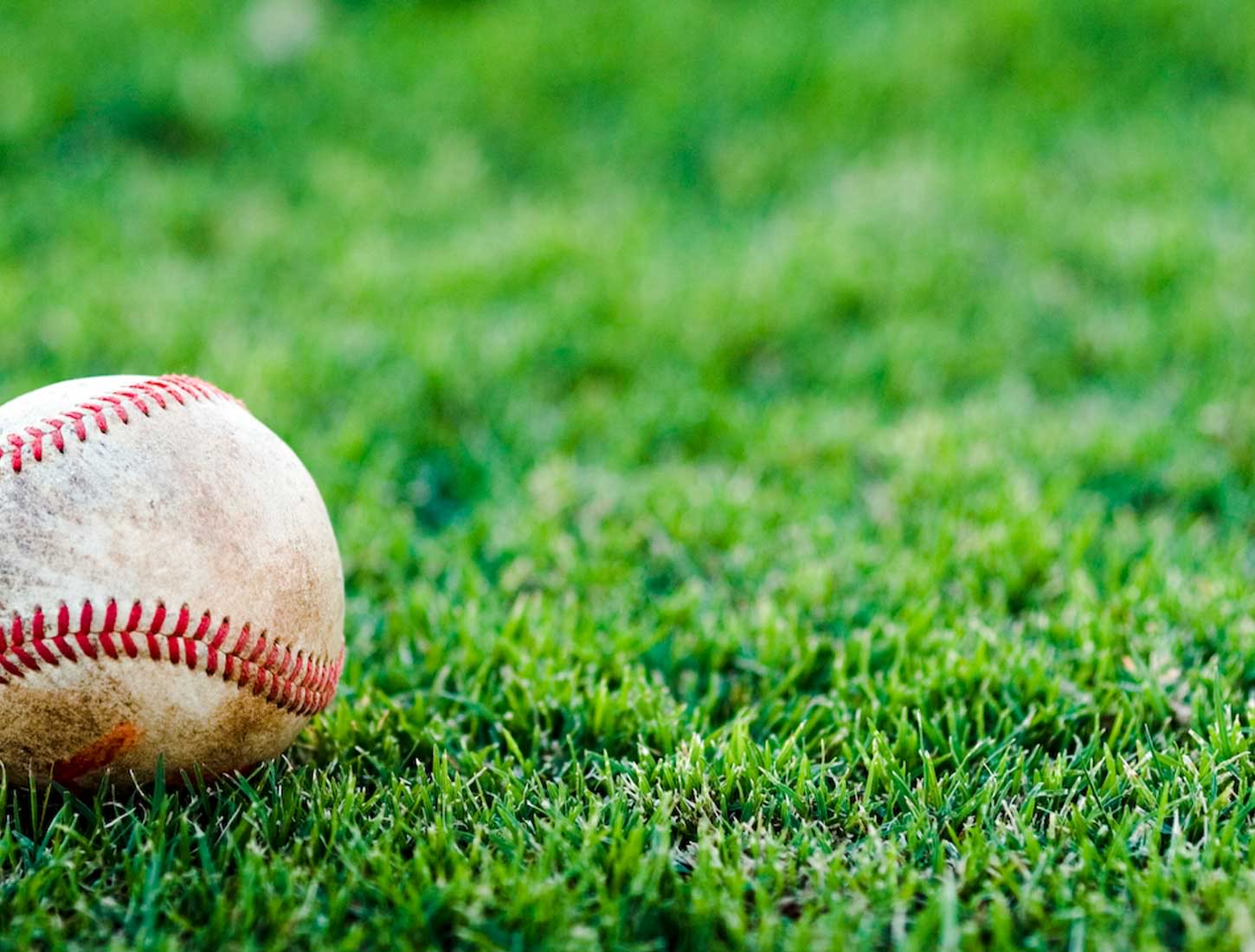 A worn baseball rests on a vibrant green grass field, evoking the spirit of America's pastime
