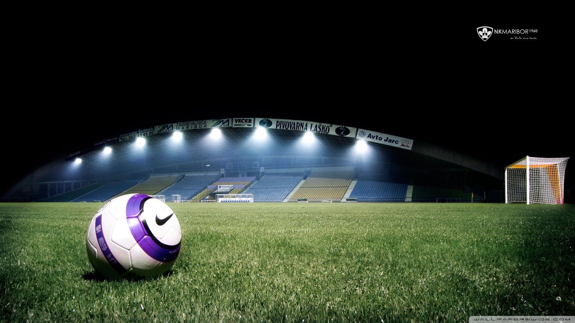 A Nike soccer ball sits on a lush green field under the bright lights of a stadium at night