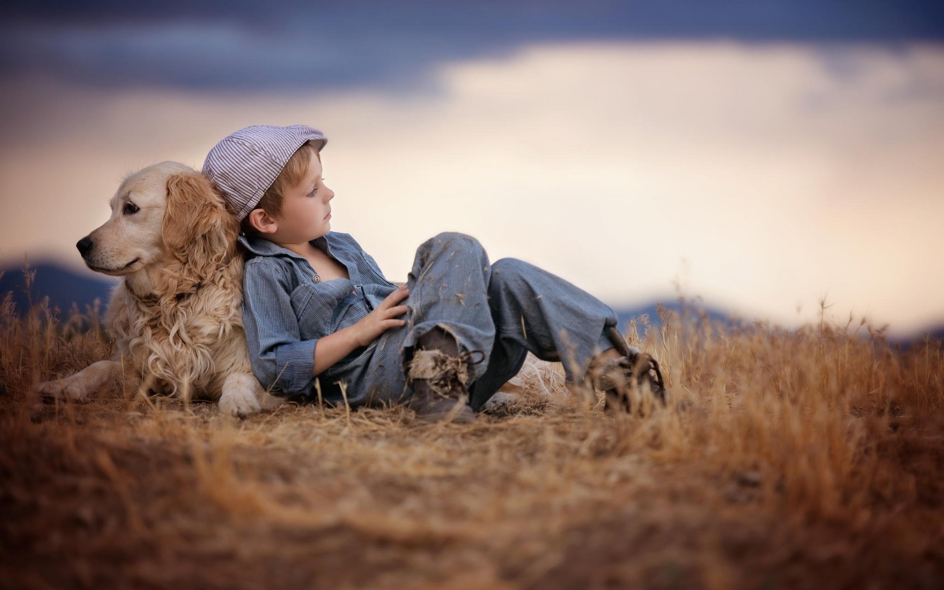 A young boy and his golden retriever dog share a peaceful moment in a field of dry grass, embodying the true essence of friendship